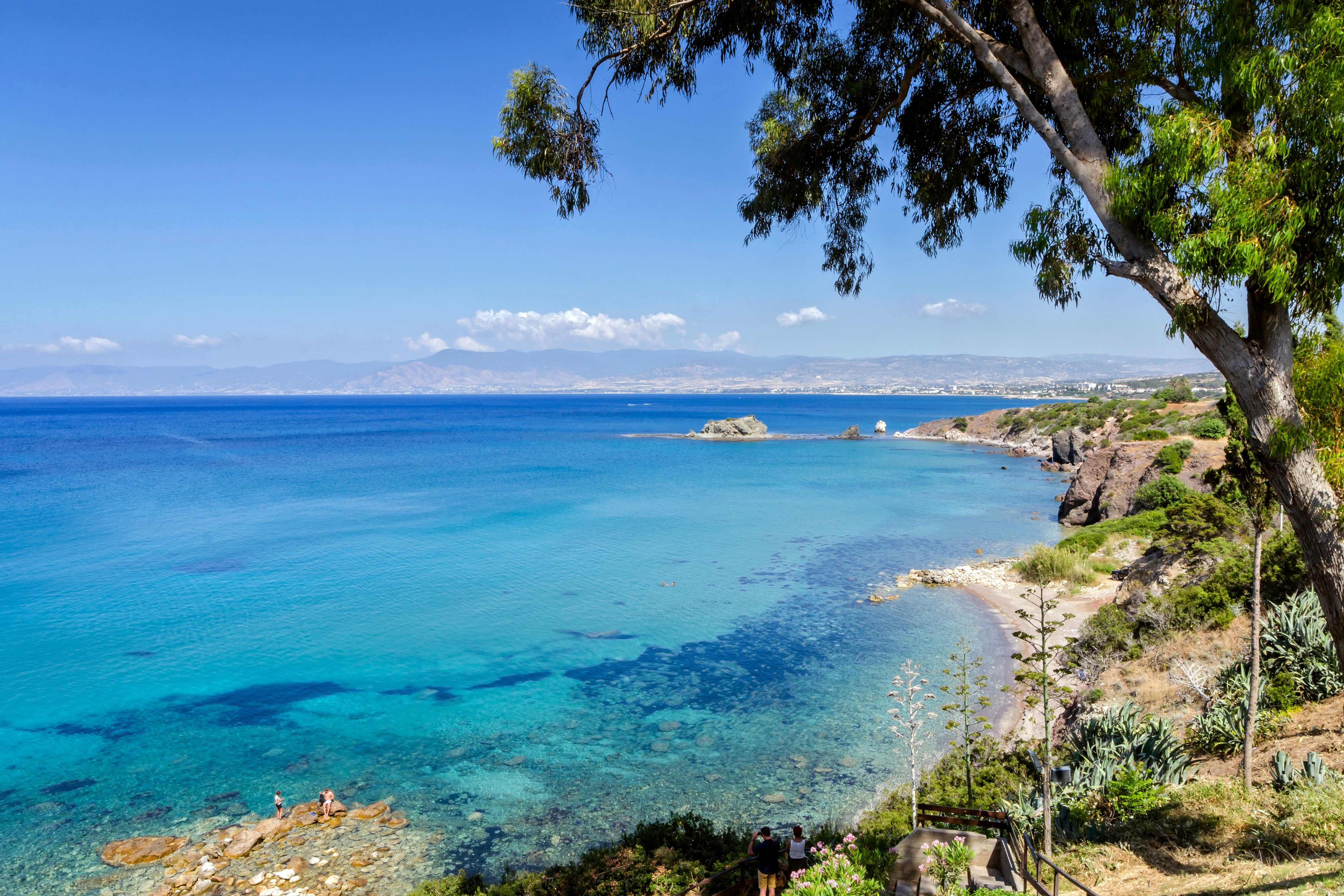 Blick auf das türkisfarbene Meer und die bewachsene Küste am Strand der Aphrodite-Bäder auf Zypern.