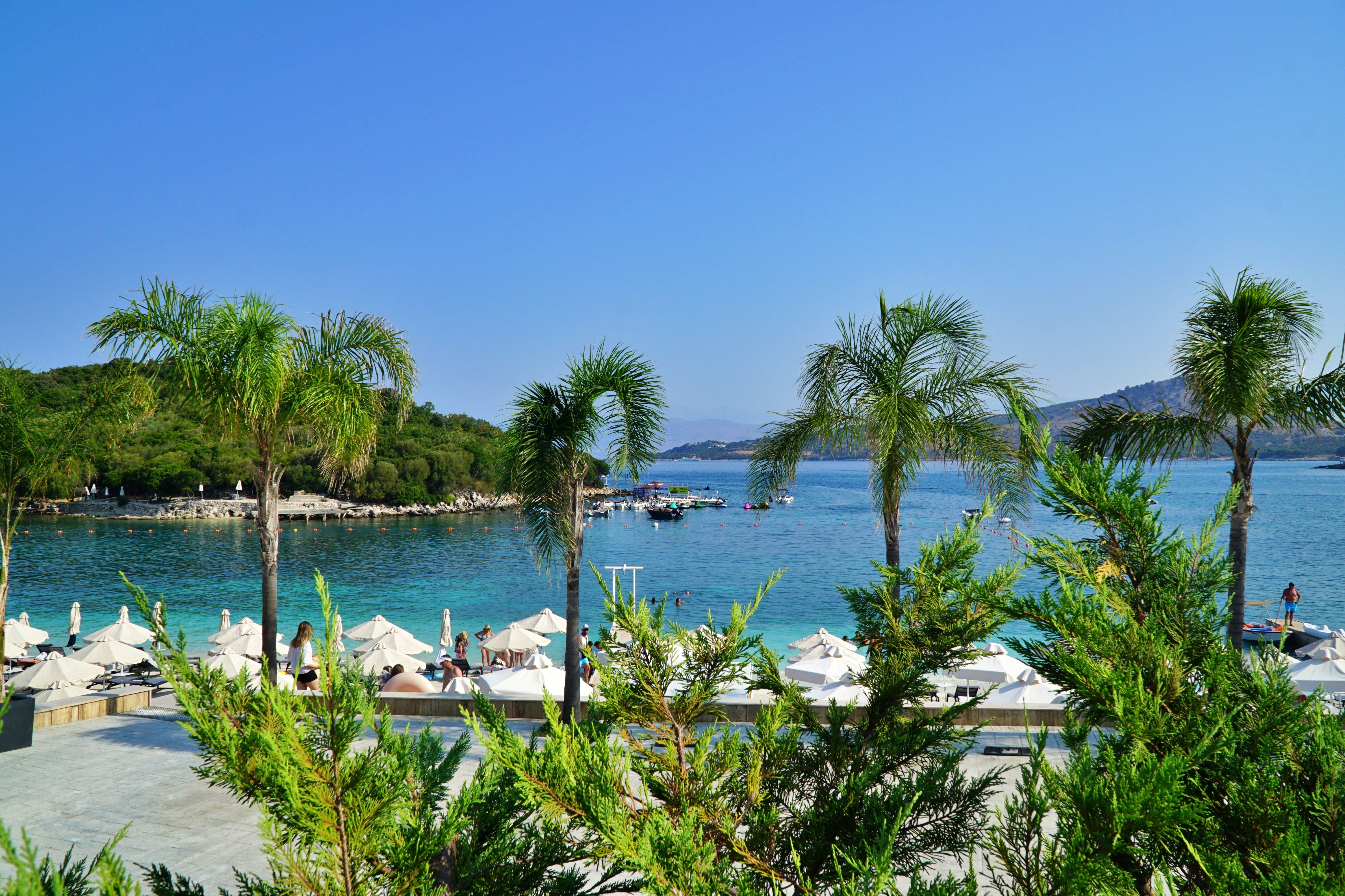 Strand in Ksamil, Albanien mit Palmen, Sonnenschirmen und klarem, blauem Meer im Hintergrund.