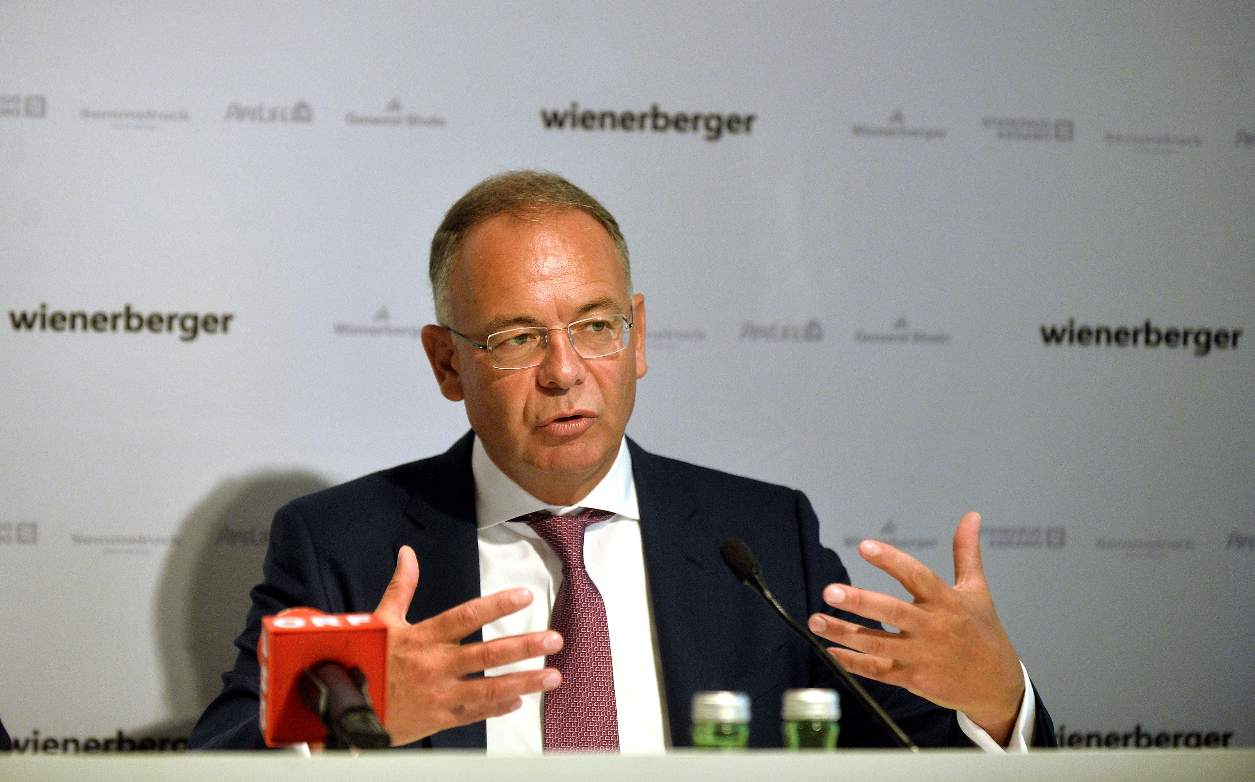 Ein Mann im Anzug spricht auf einer Pressekonferenz vor einem Wienerberger-Hintergrund.