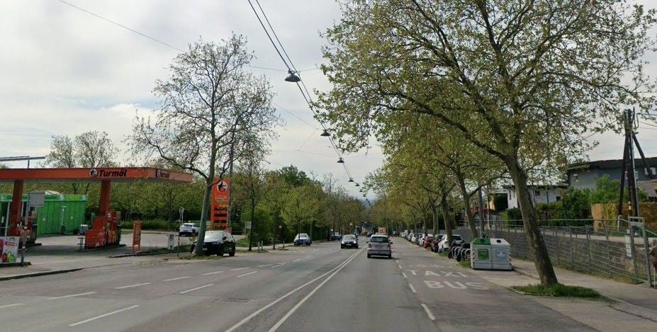 Straßenszene mit Tankstelle, Autos und Bäumen entlang der Laaerberg Straße in Wien.