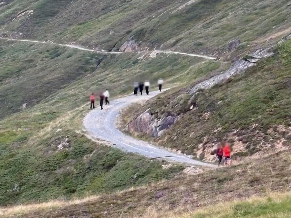 Mehrere Wanderer gehen auf einem kurvigen Weg durch hügeliges, grünes Gebirge.