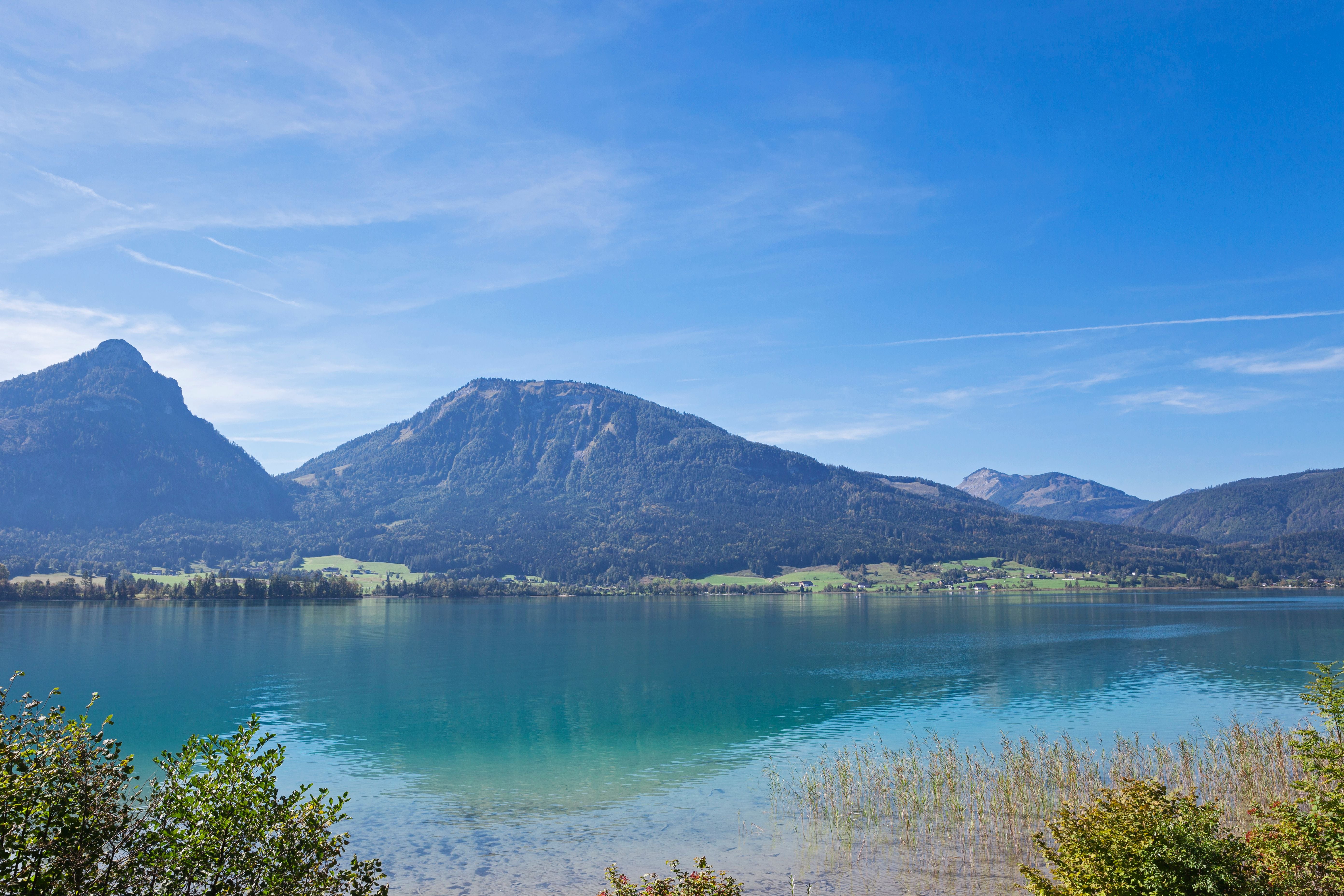 Klarer Wolfgangsee mit spiegelndem Wasser, umgeben von bewaldeten Bergen und blauem Himmel.