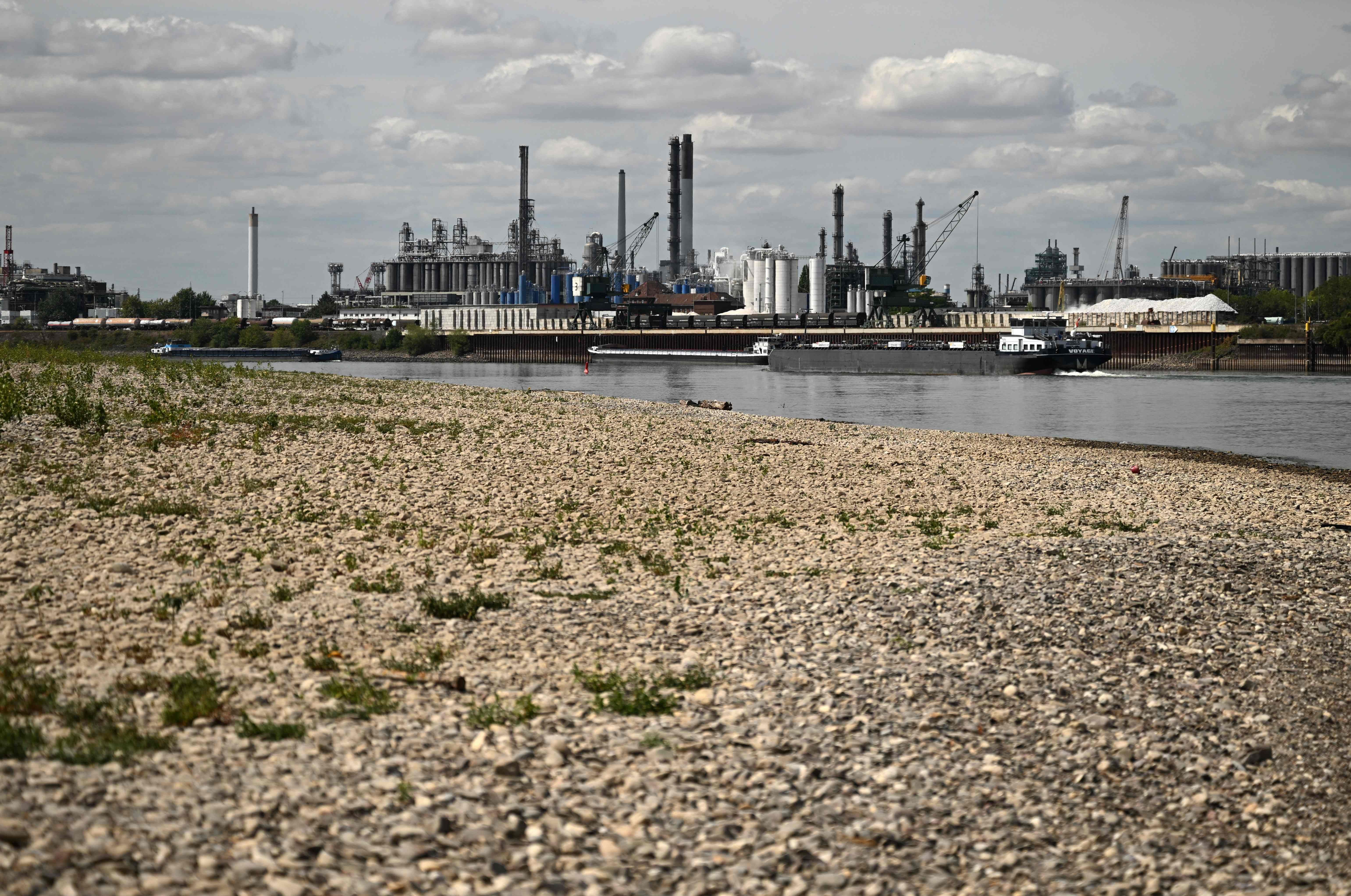 Ein Frachtschiff passiert ein teilweise ausgetrocknetes Rheinufer vor Industrieanlagen bei Köln.
