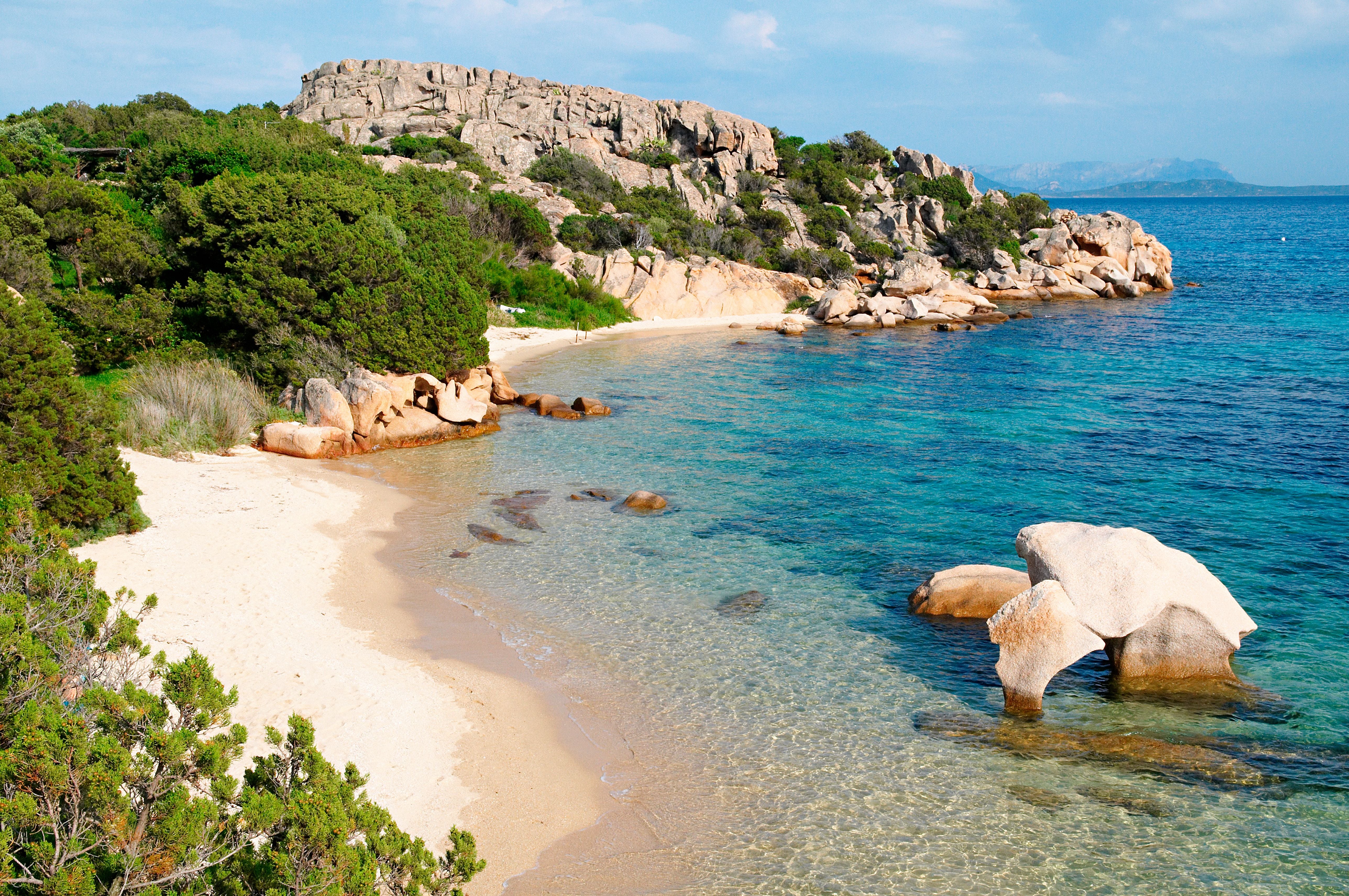 Klarer Sandstrand mit Felsen und türkisblauem Wasser an der Küste Sardiniens.