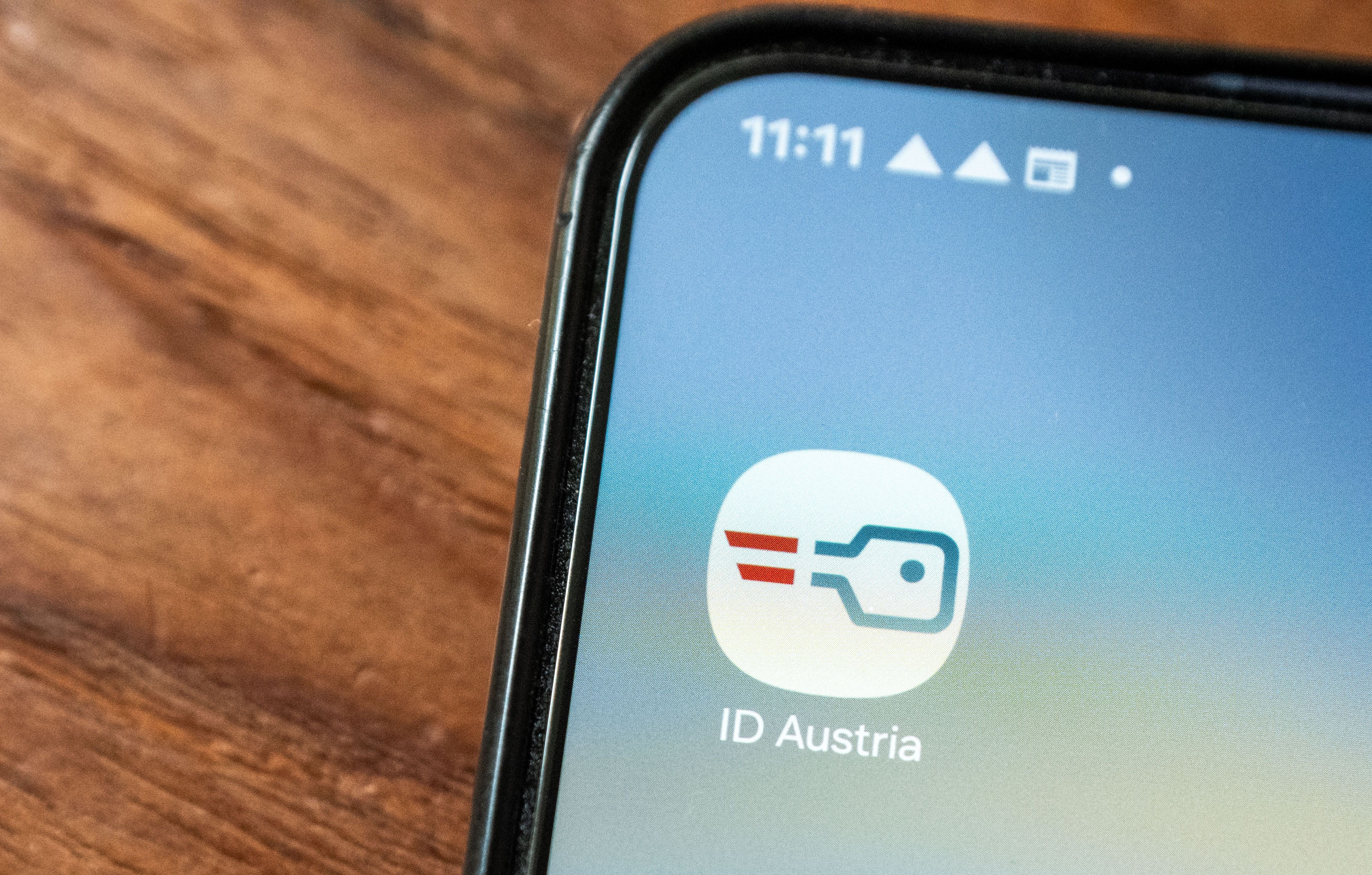 Smartphone mit aufgerufenem App-Symbol "ID Austria" auf Holzoberfläche.