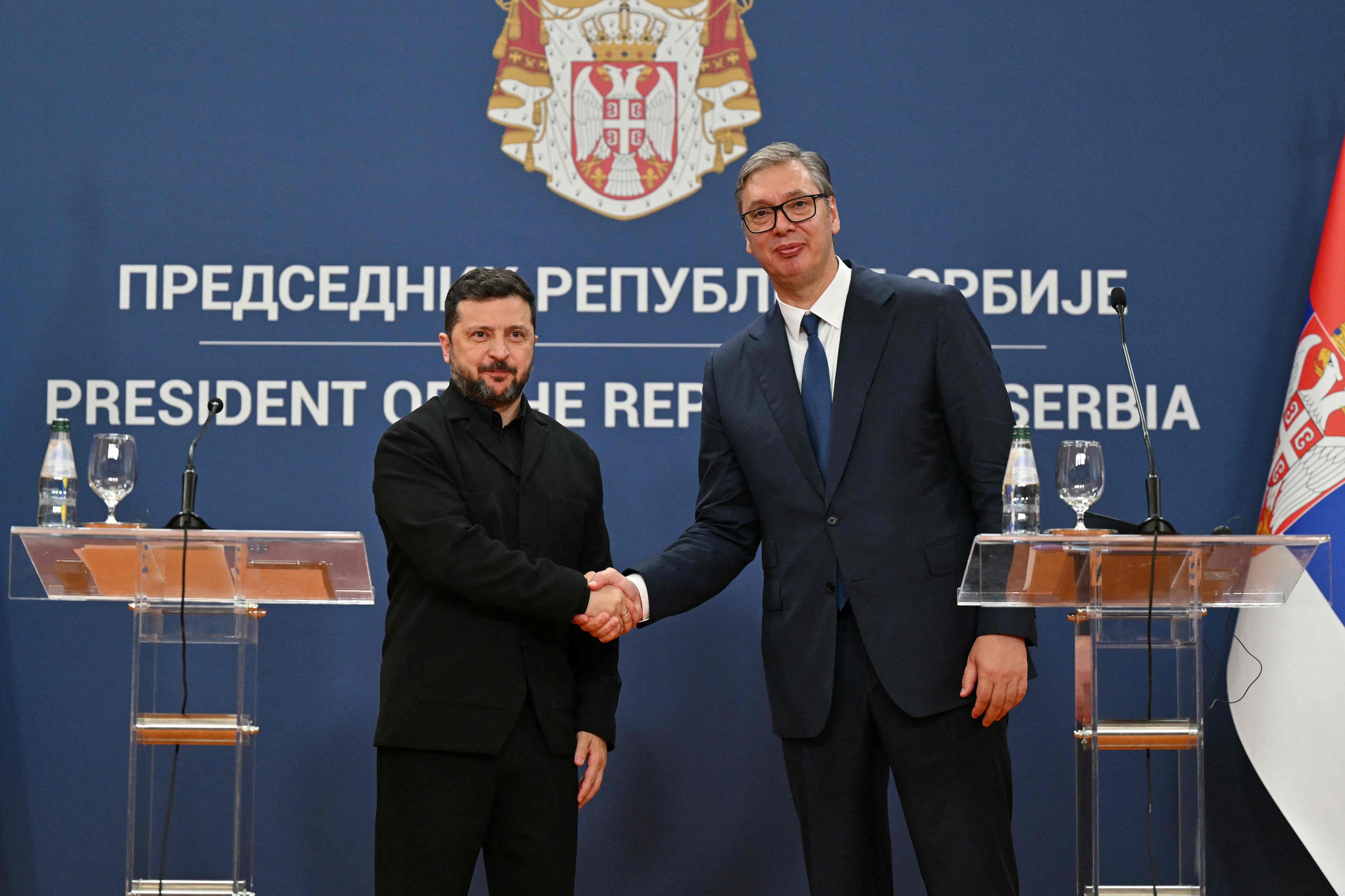 Zwei Männer geben sich bei einer Pressekonferenz in Belgrad die Hand vor serbischer Flagge.