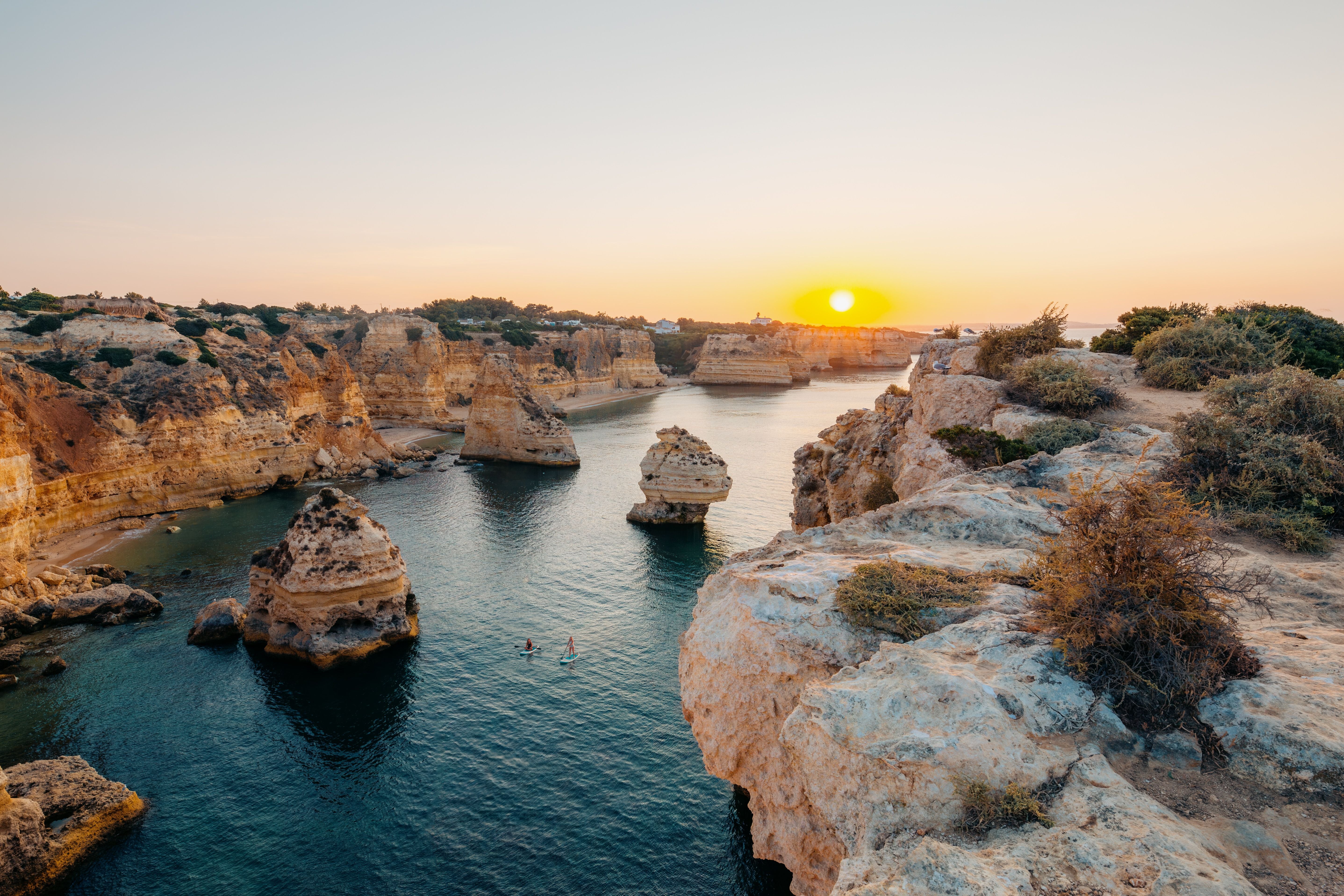 Sonnenuntergang an der Algarve-Küste mit Touristen auf Stand-Up-Paddleboards im Wasser.