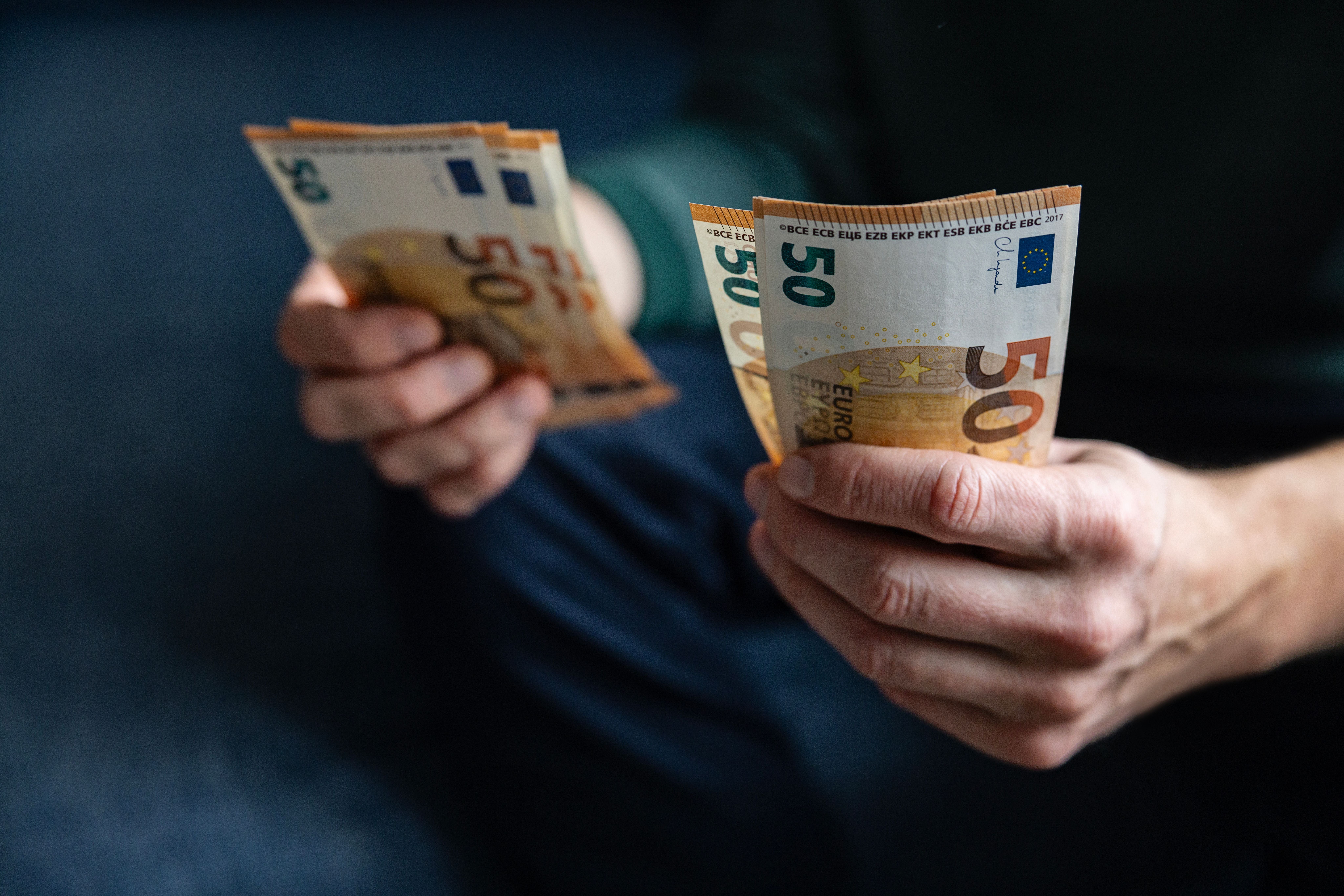 Eine Person zählt mehrere 50-Euro-Geldscheine mit beiden Händen.