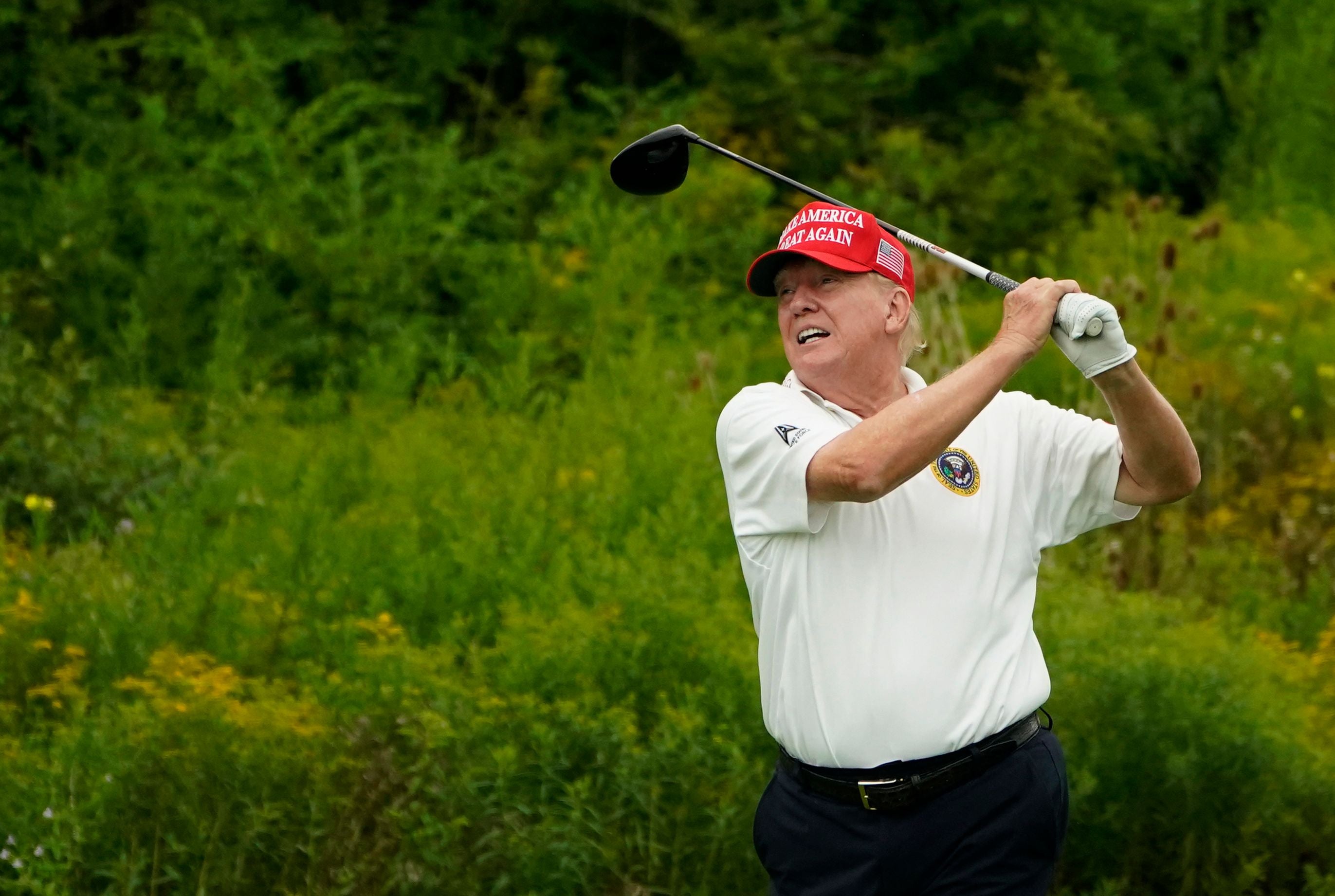 Ein Mann mit rotem Basecap spielt Golf auf einem grünen Golfplatz.