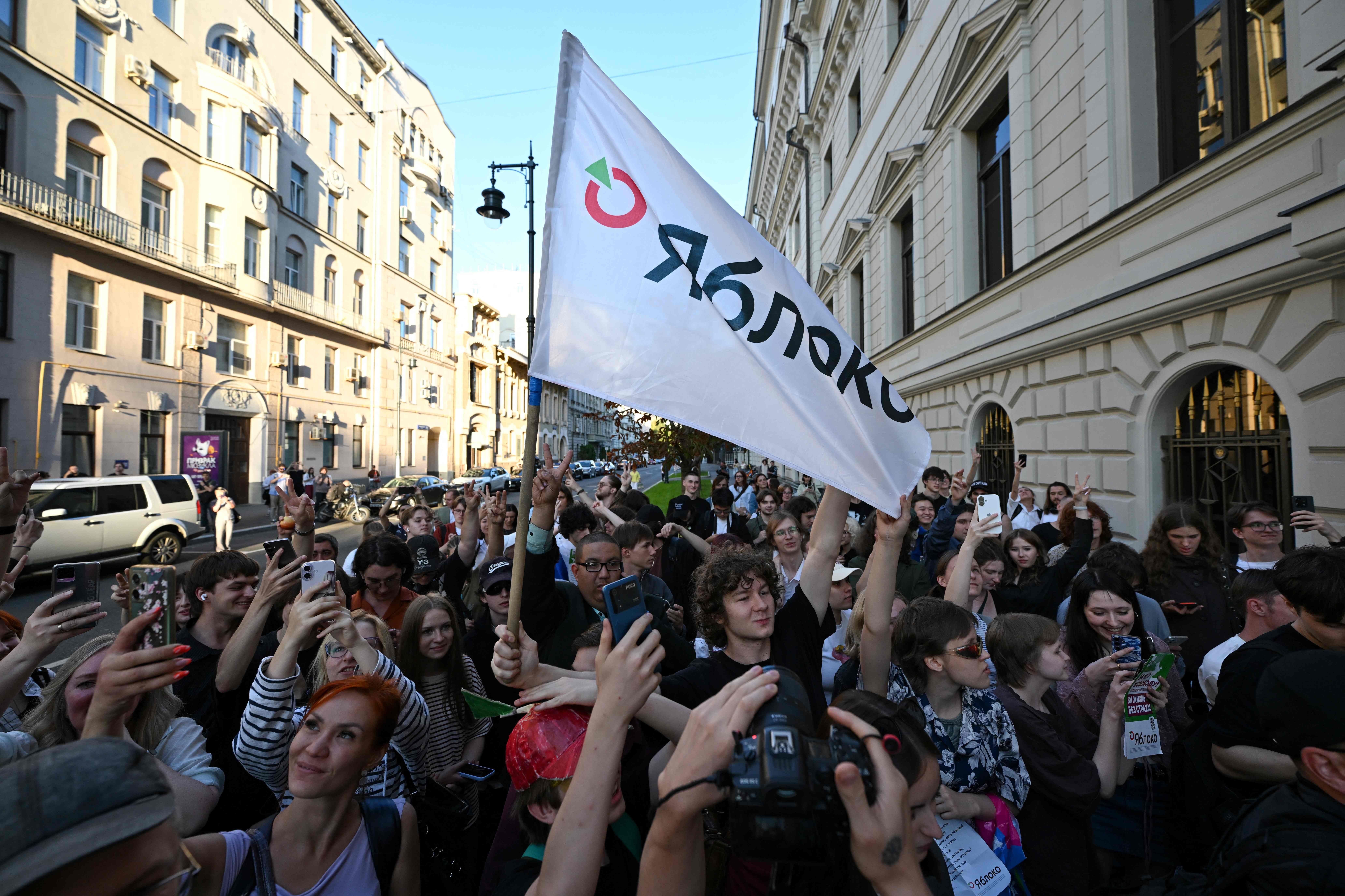 Menschenmenge hält eine Jabloko-Flagge vor einem Gebäude in Moskau, viele fotografieren mit Handys.