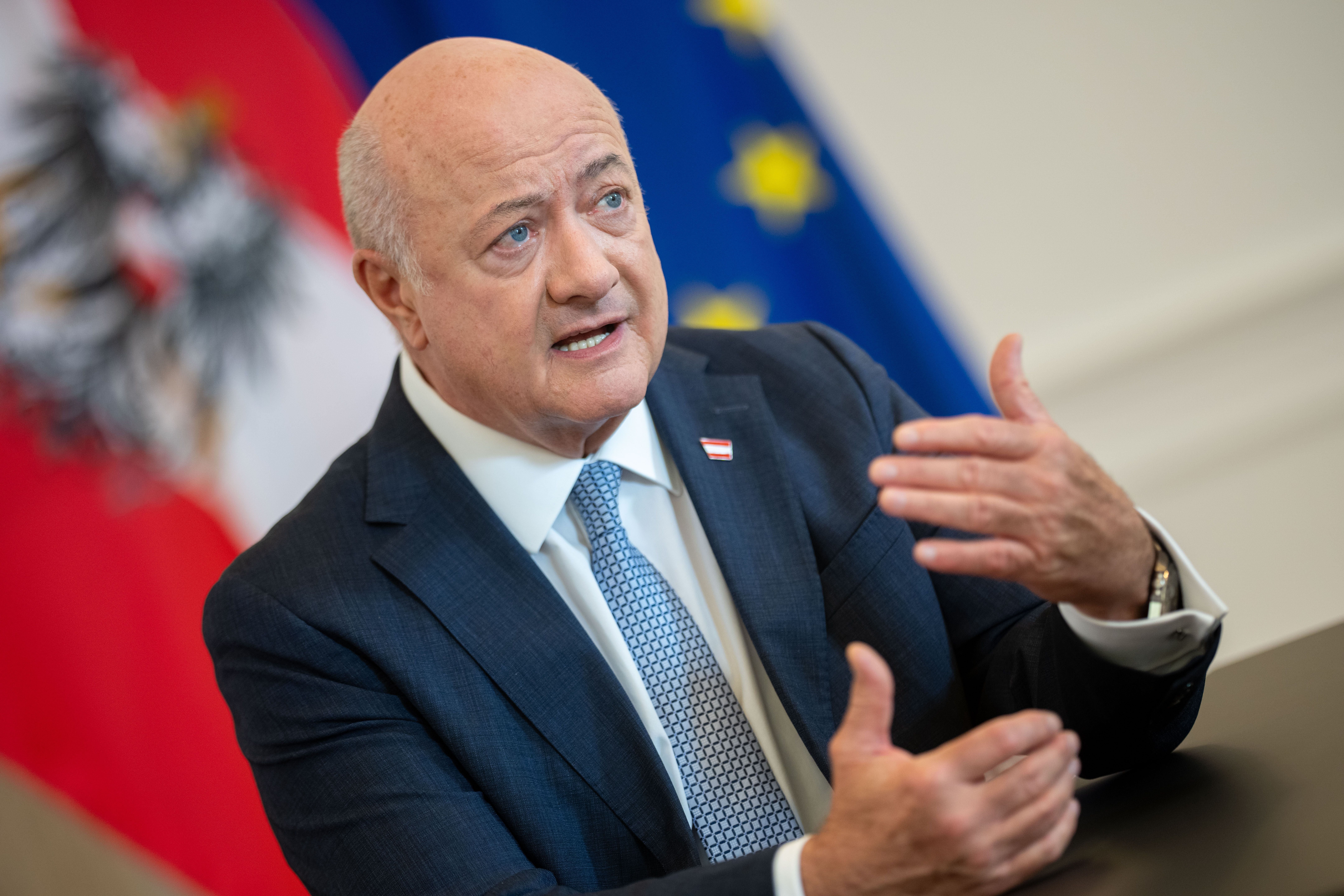 Ein Mann im Anzug spricht gestikulierend vor österreichischer und EU-Flagge.