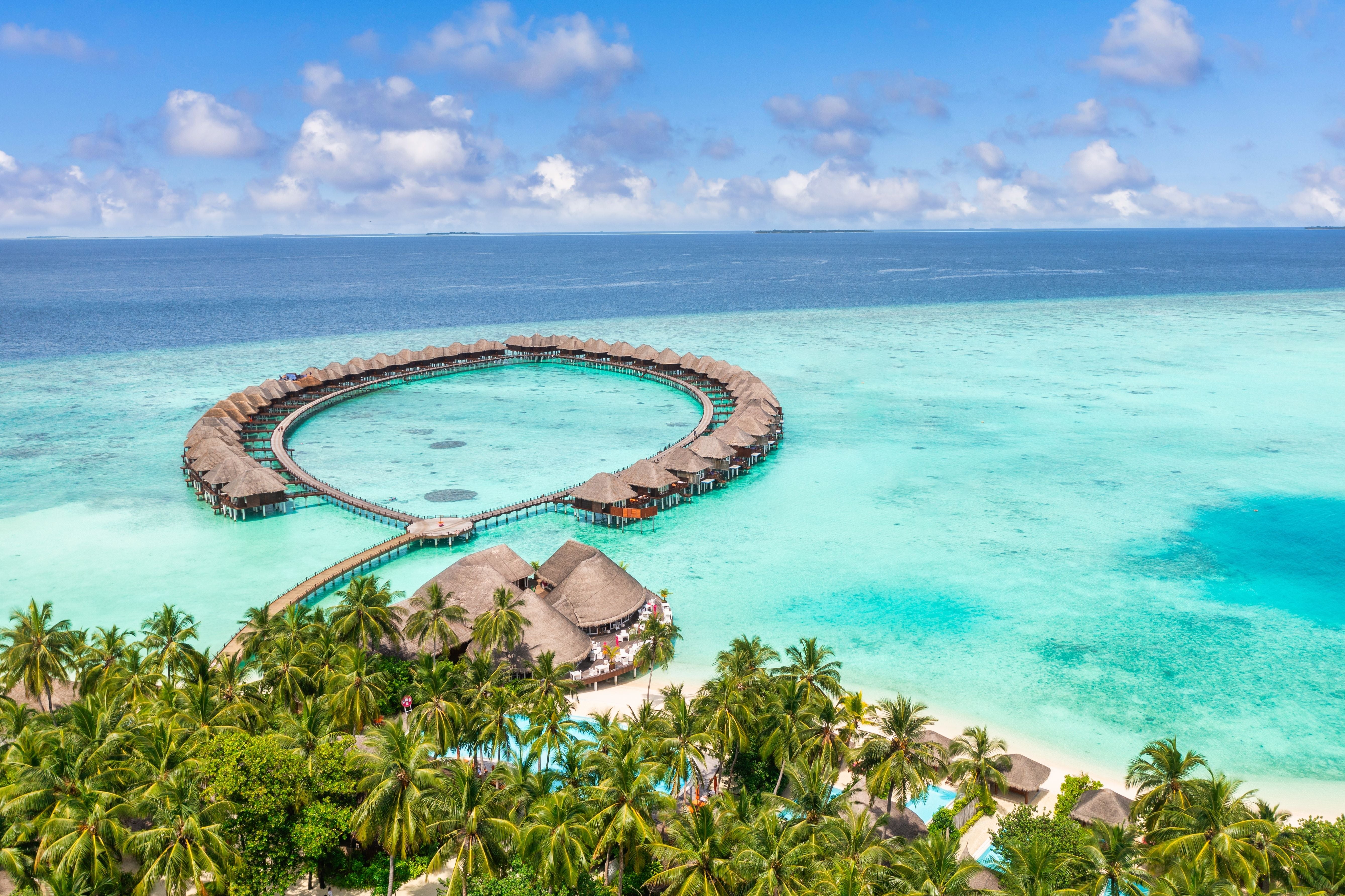 Luftaufnahme einer tropischen Insel mit Palmen, weißen Stränden und runden Wasser-Villen im türkisfarbenen Meer.