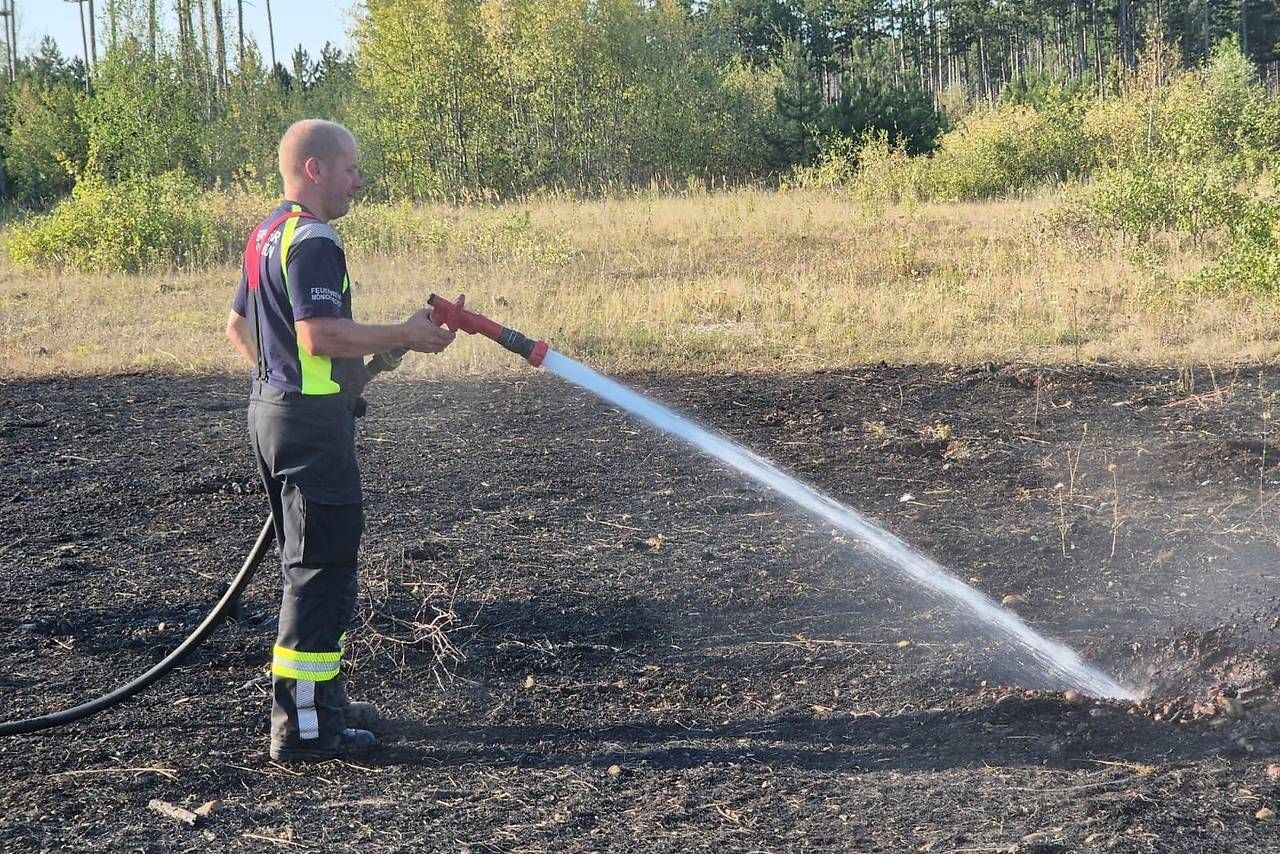 Ein Feuerwehrmann löscht mit einem Schlauch Glutnester auf einem abgebrannten Feld.
