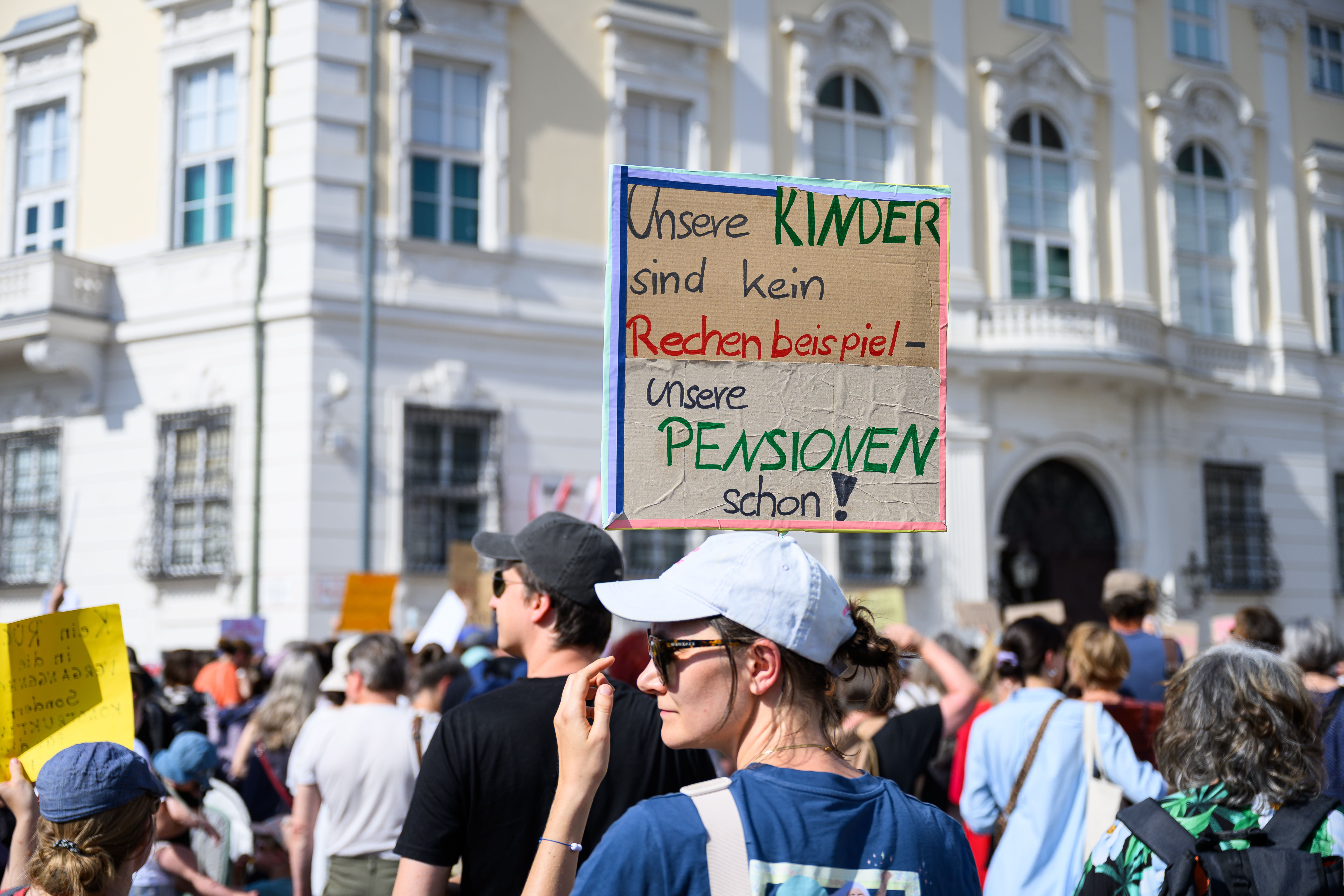 Frau hält Schild bei einer Demonstration in Wien mit vielen Menschen im Hintergrund.