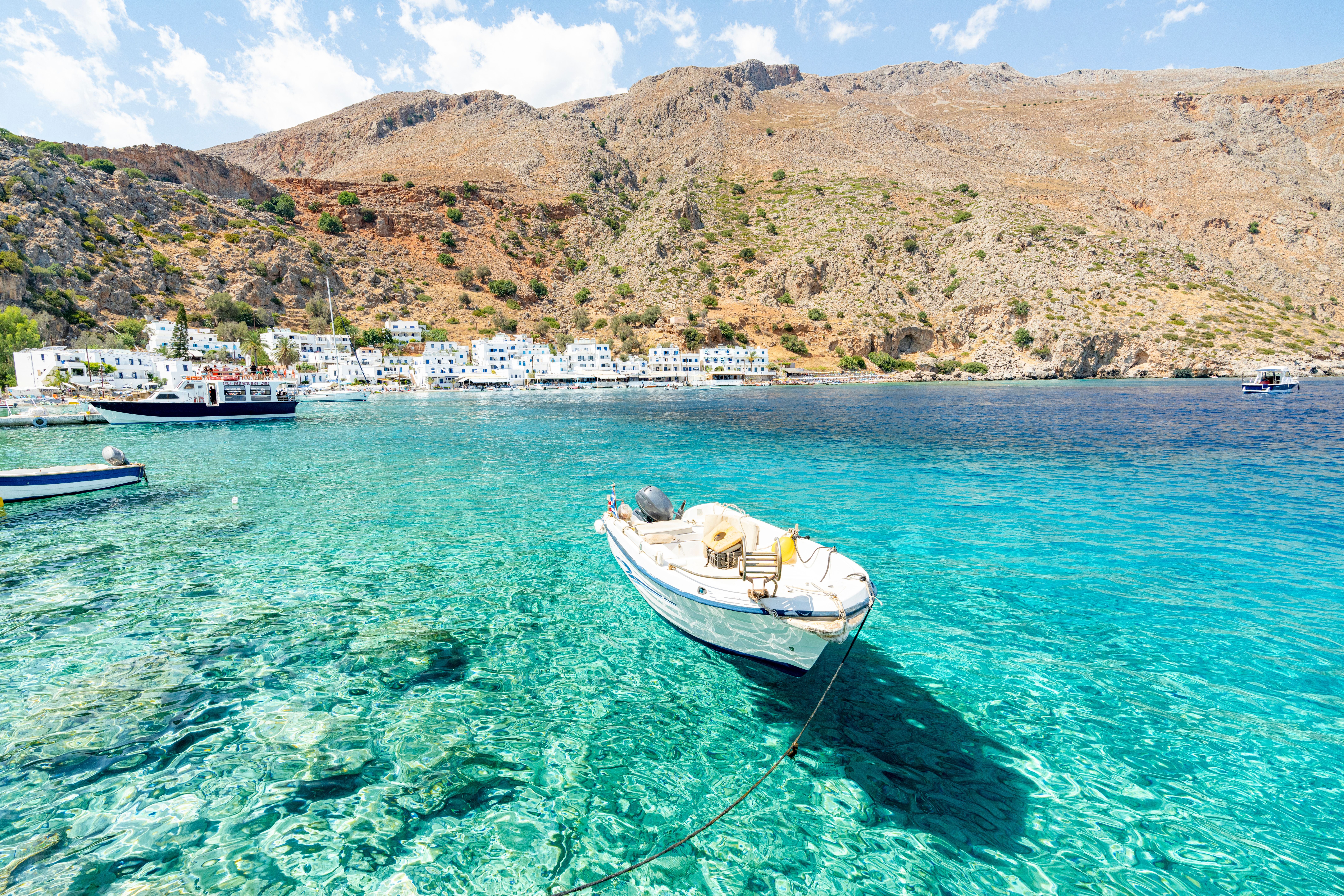 Kleines Boot schwimmt auf kristallklarem Wasser vor dem Küstenort Loutro auf Kreta, Griechenland.
