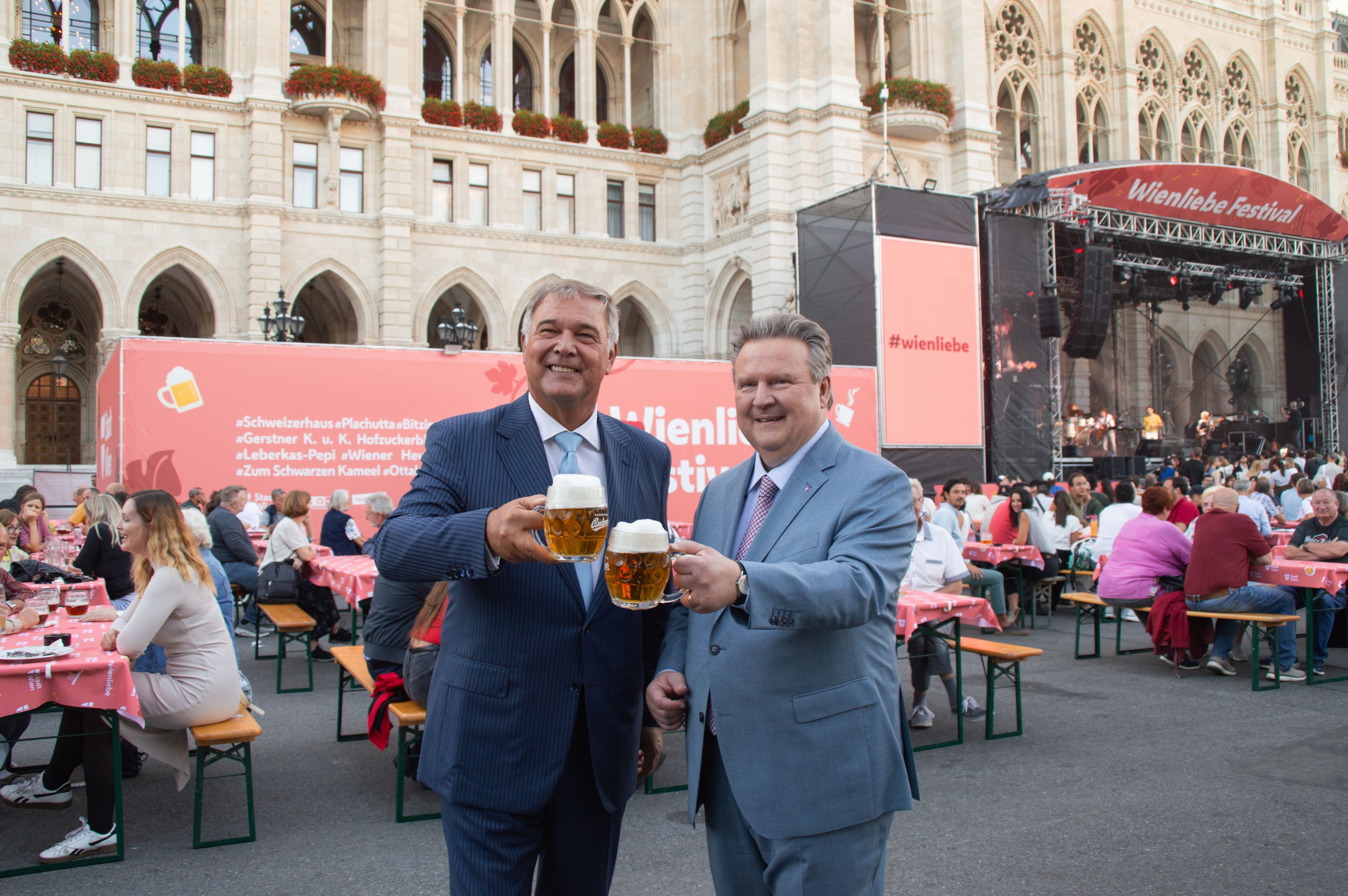 Zwei Männer stoßen mit Biergläsern vor dem Wienliebe Festival am Rathausplatz an.
