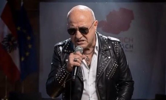 KI-Video zeigt: Bundeskanzler Stocker in Lederjacke und Sonnenbrille singt in ein Mikrofon.