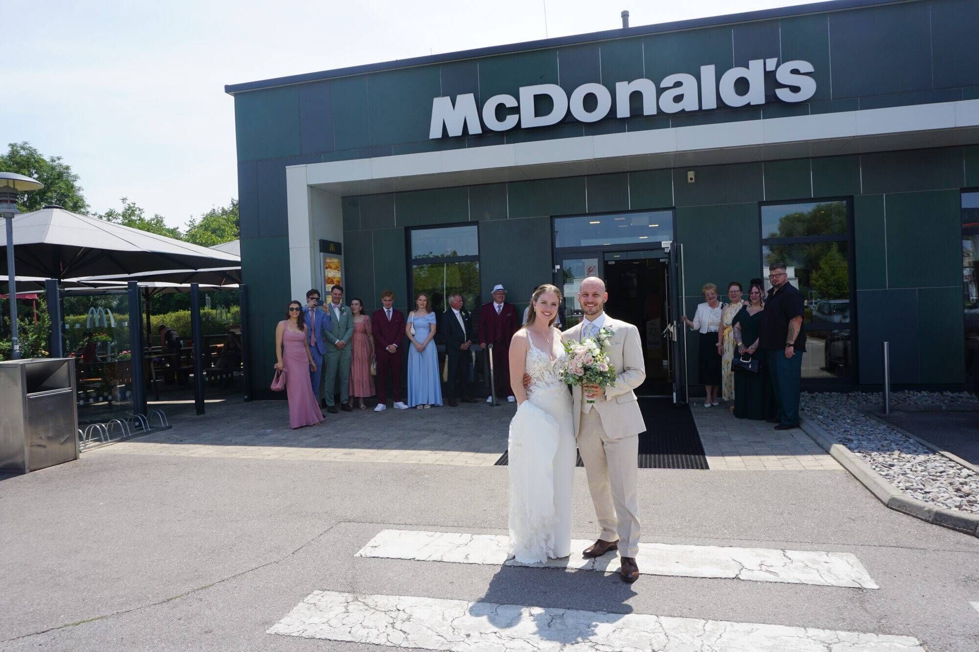 Brautpaar posiert vor dem Hollabrunner McDonald's-Restaurant, Hochzeitsgäste stehen im Hintergrund.