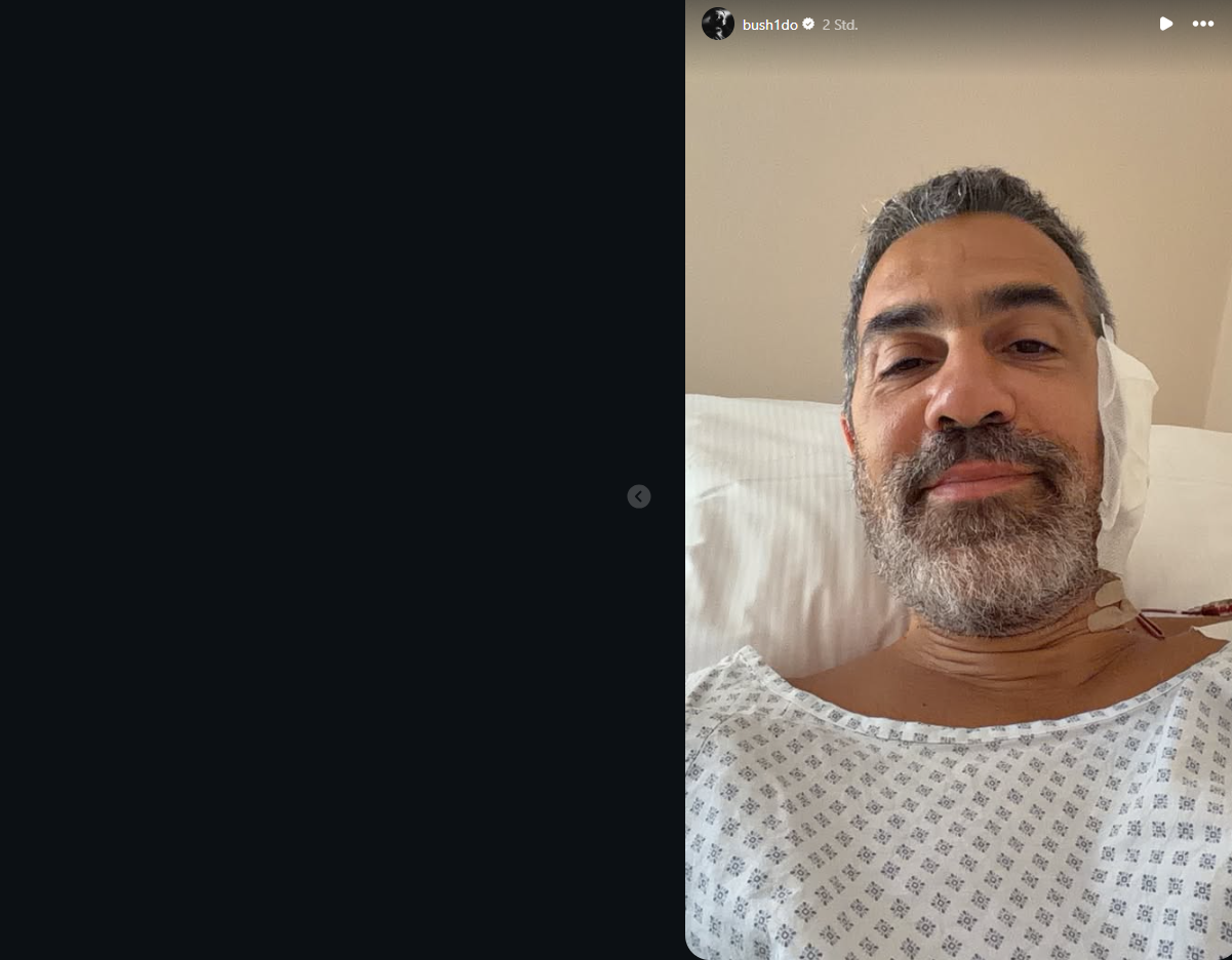 Ein Mann mit Bart liegt in einem Krankenhausbett und trägt ein Patientenhemd.
