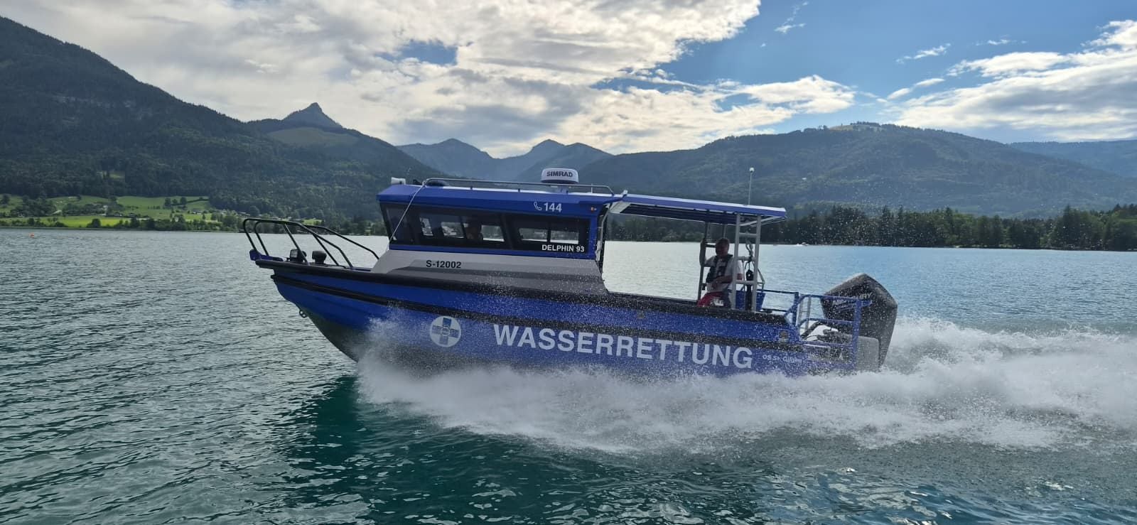 Ein Wasserrettungsboot fährt schnell auf dem Wolfgangsee, im Hintergrund Berge und Wälder.