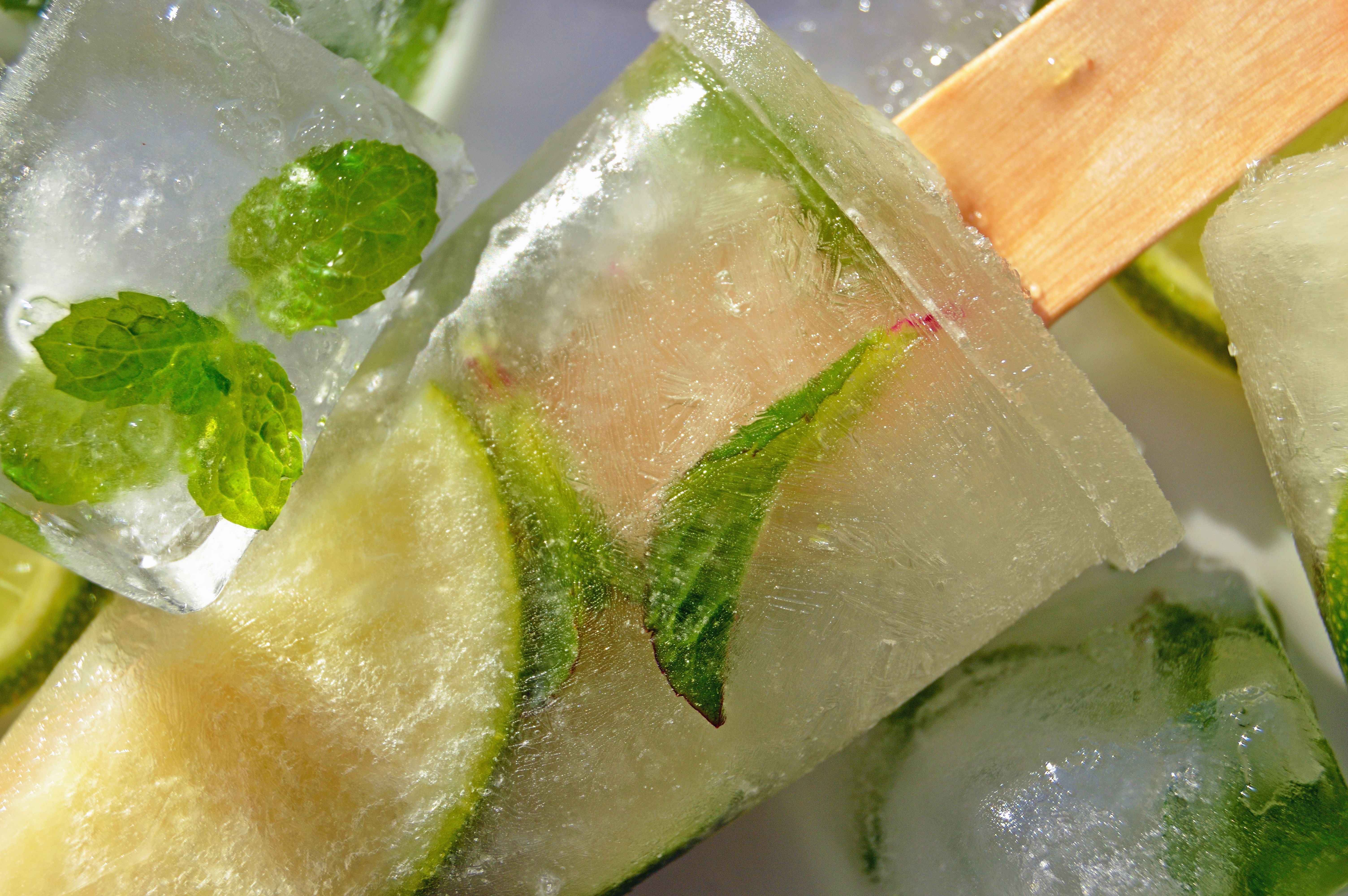 Gefrorenes Hugo-Eis am Stiel mit Limettenscheiben und frischer Minze, umgeben von Eiswürfeln.