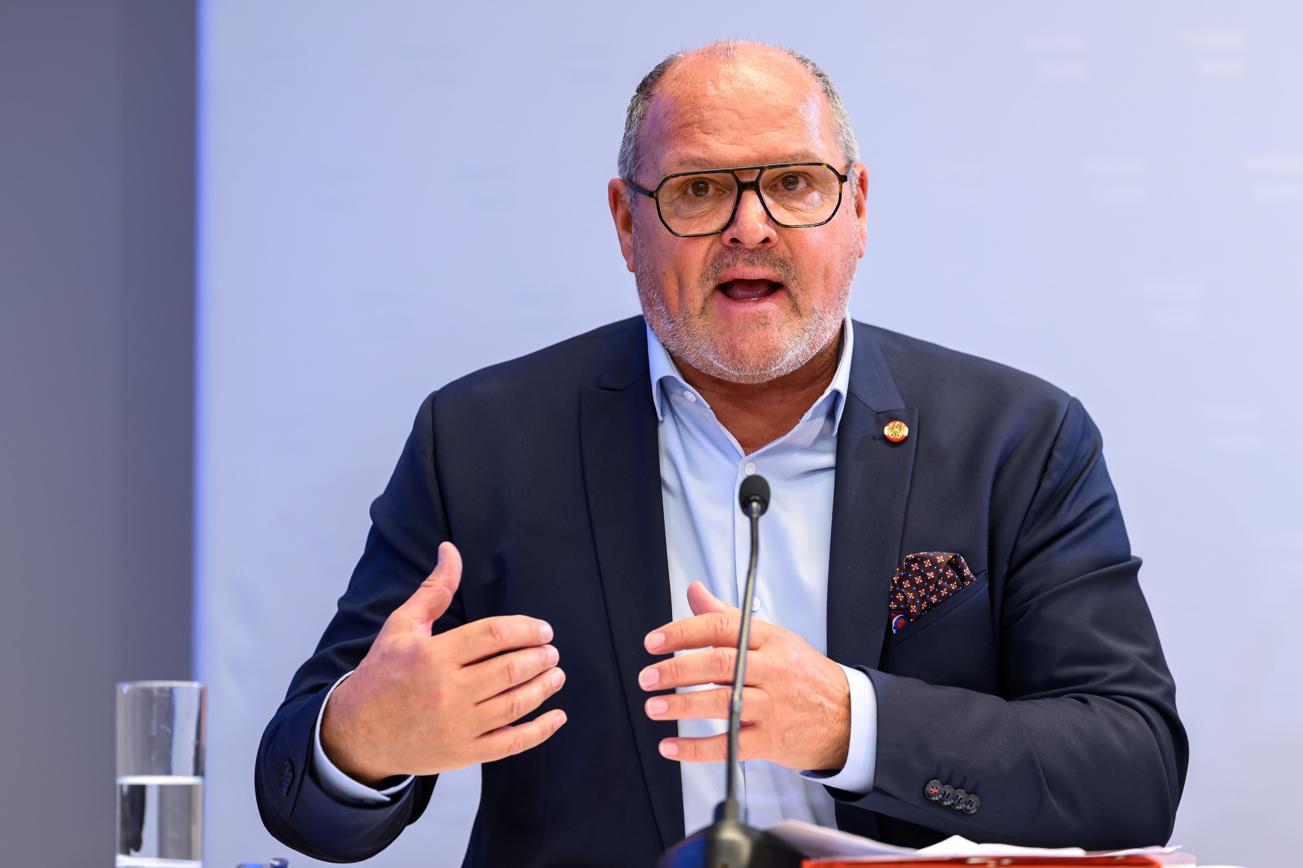 Ein Mann im Anzug spricht auf einer Pressekonferenz vor einem Mikrofon.