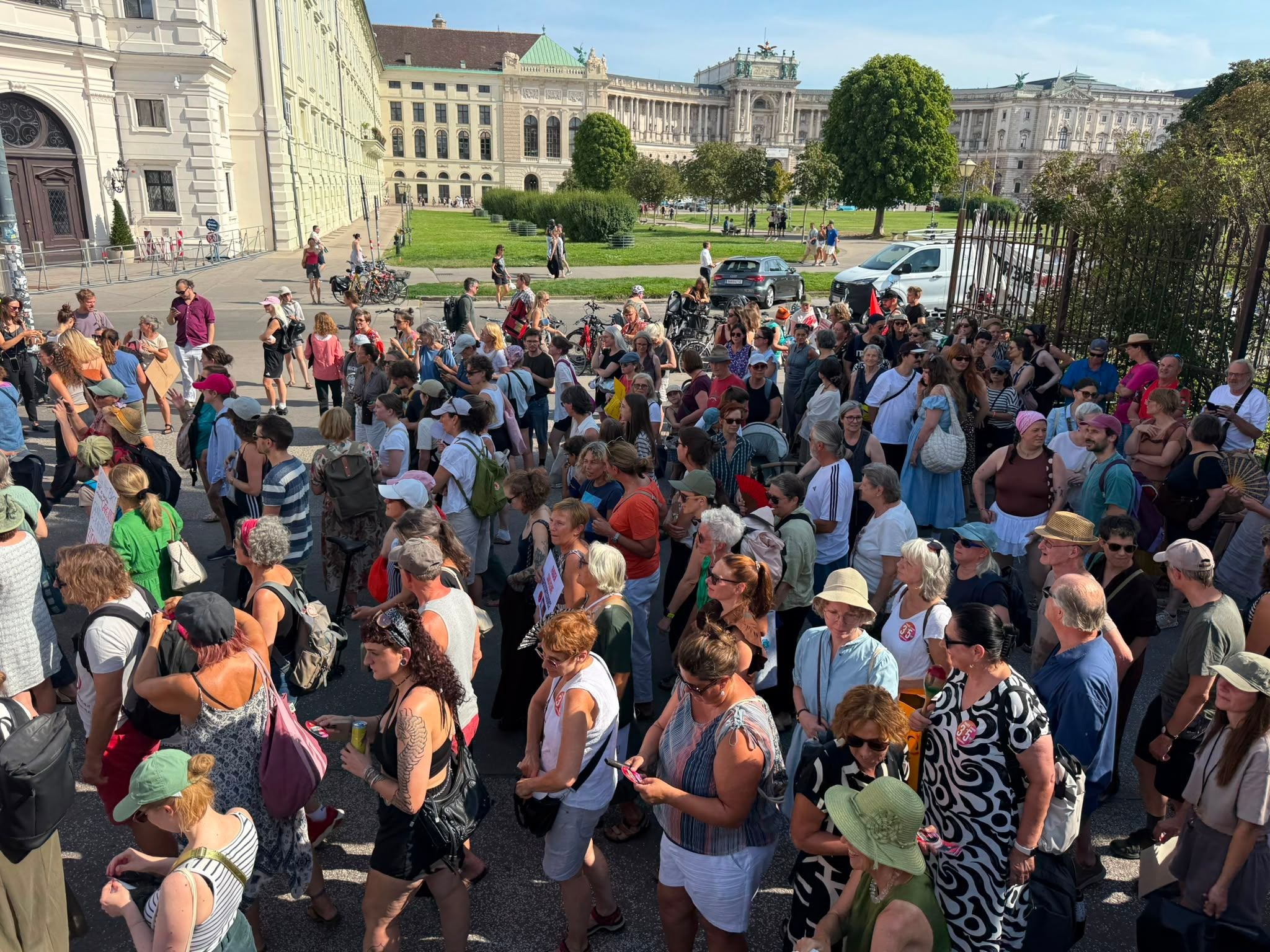 Große Gruppe von Menschen versammelt sich bei Sonnenschein zu einer Frauen-Demo in einer Stadt.