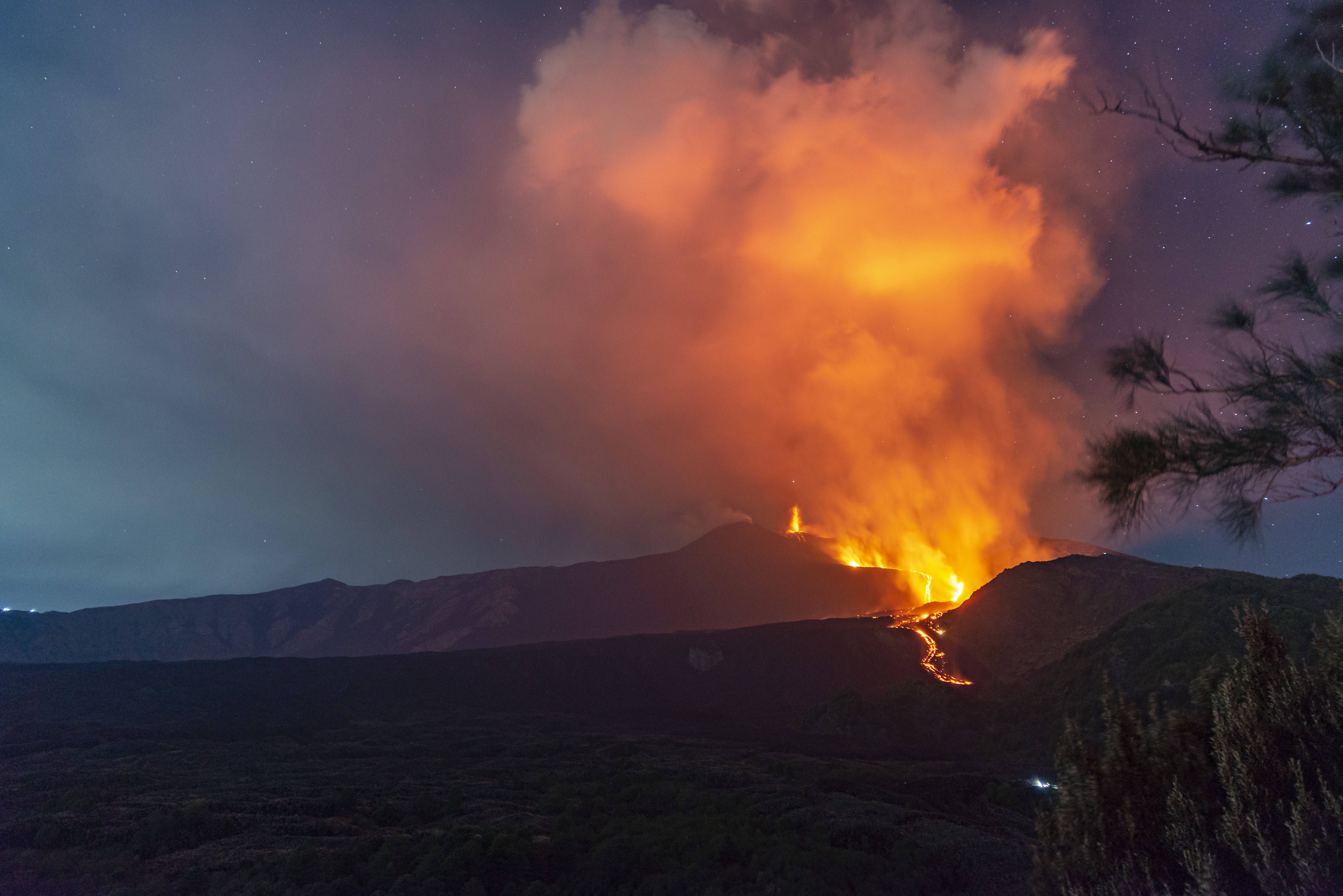 Ein nächtlicher Vulkanausbruch mit glühender Lava und dichter Aschewolke am Himmel.