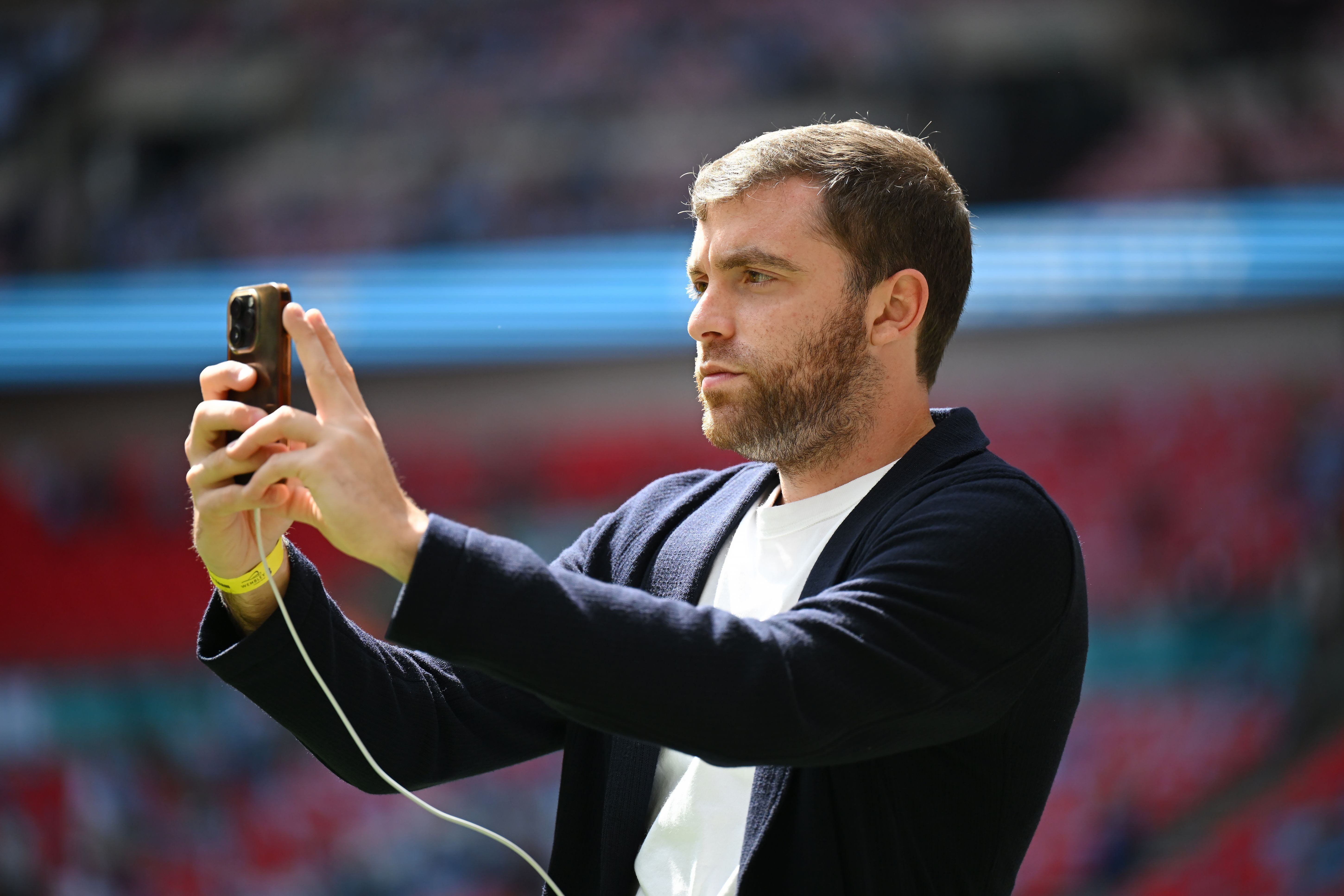 Ein Mann hält ein Smartphone und macht ein Foto im Fußballstadion.