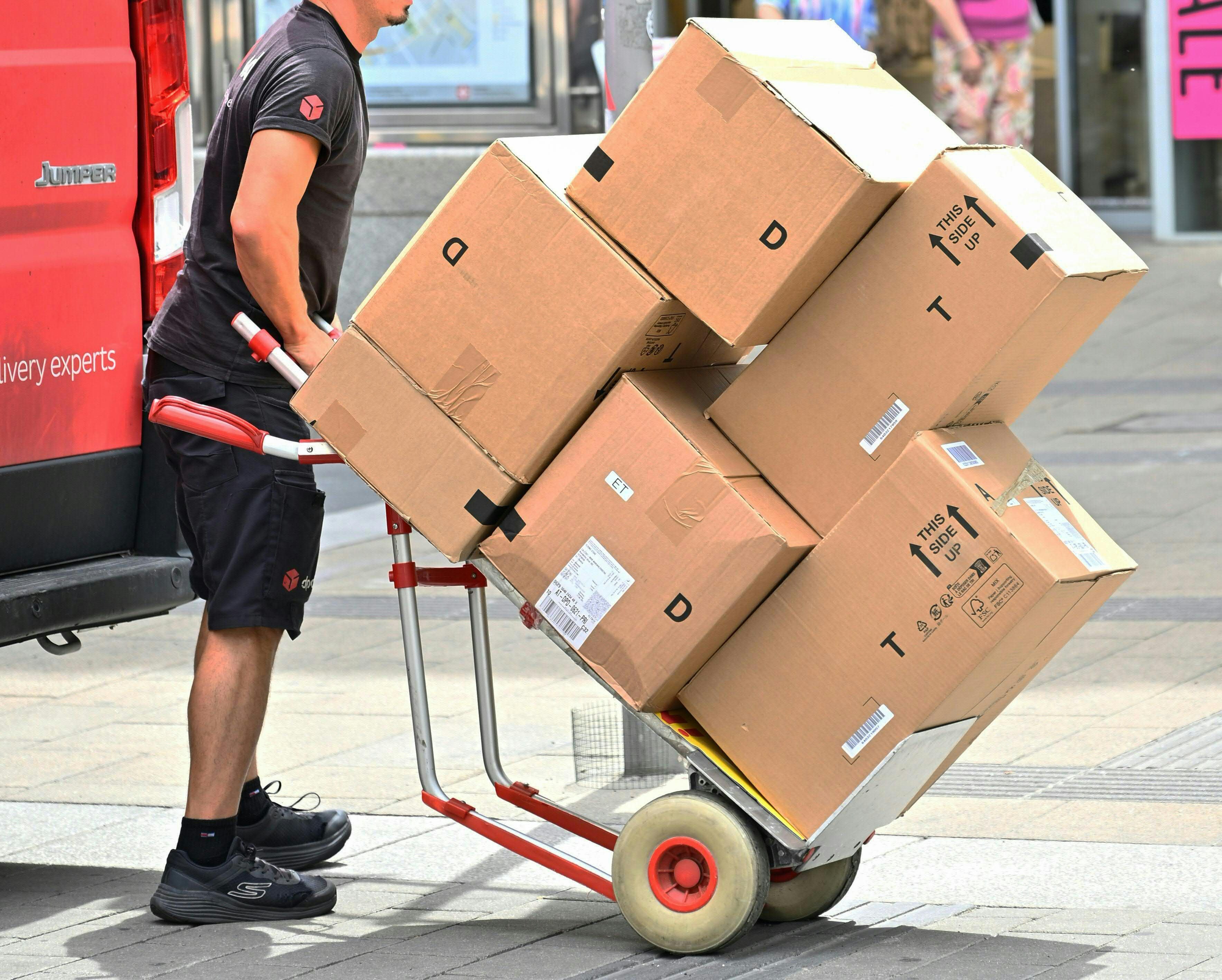 Ein Paketzusteller transportiert mehrere Kartons auf einer Sackkarre durch die Stadt.