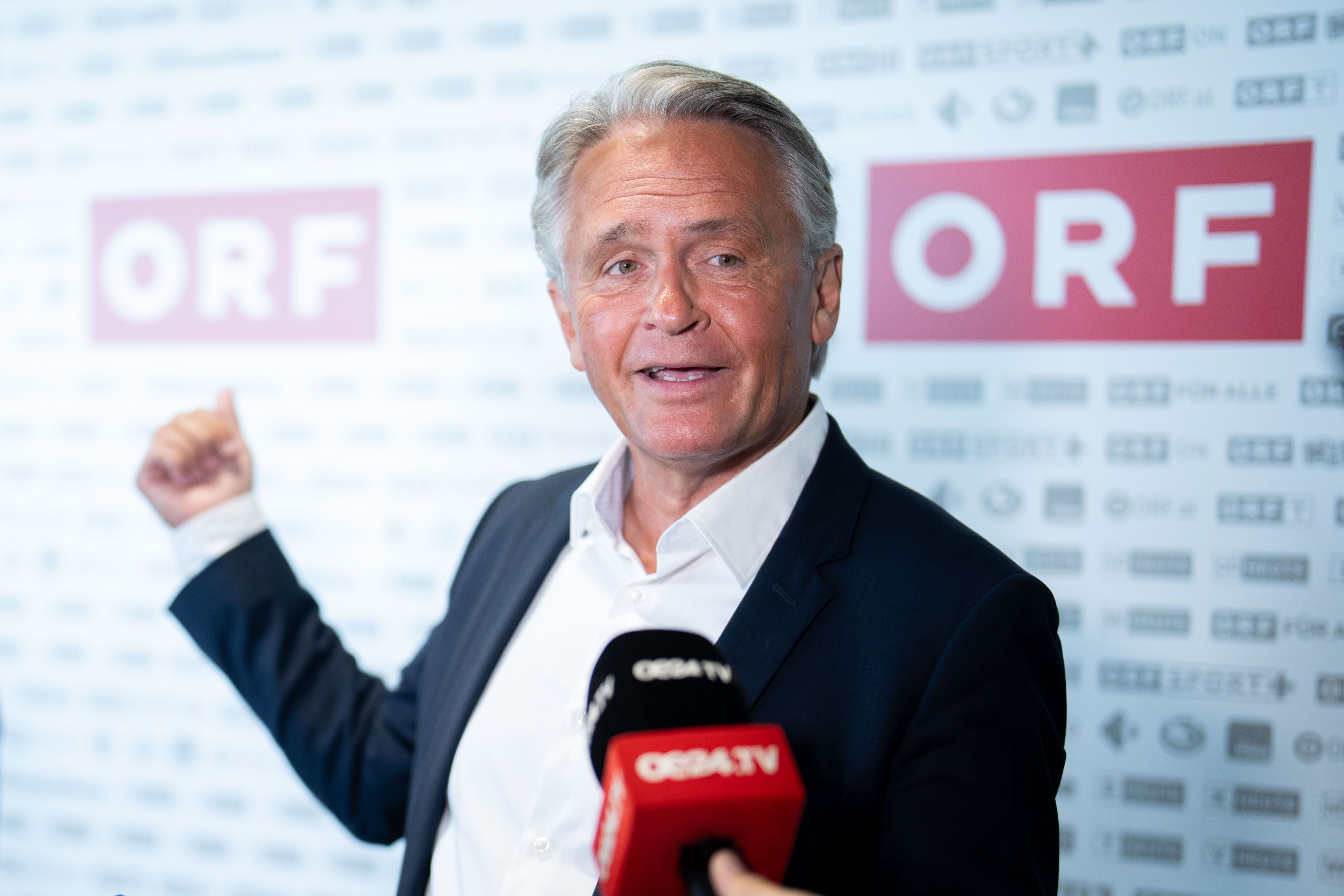 Ein Mann im Anzug spricht vor ORF-Logos und Mikrofonen bei einer Pressekonferenz.