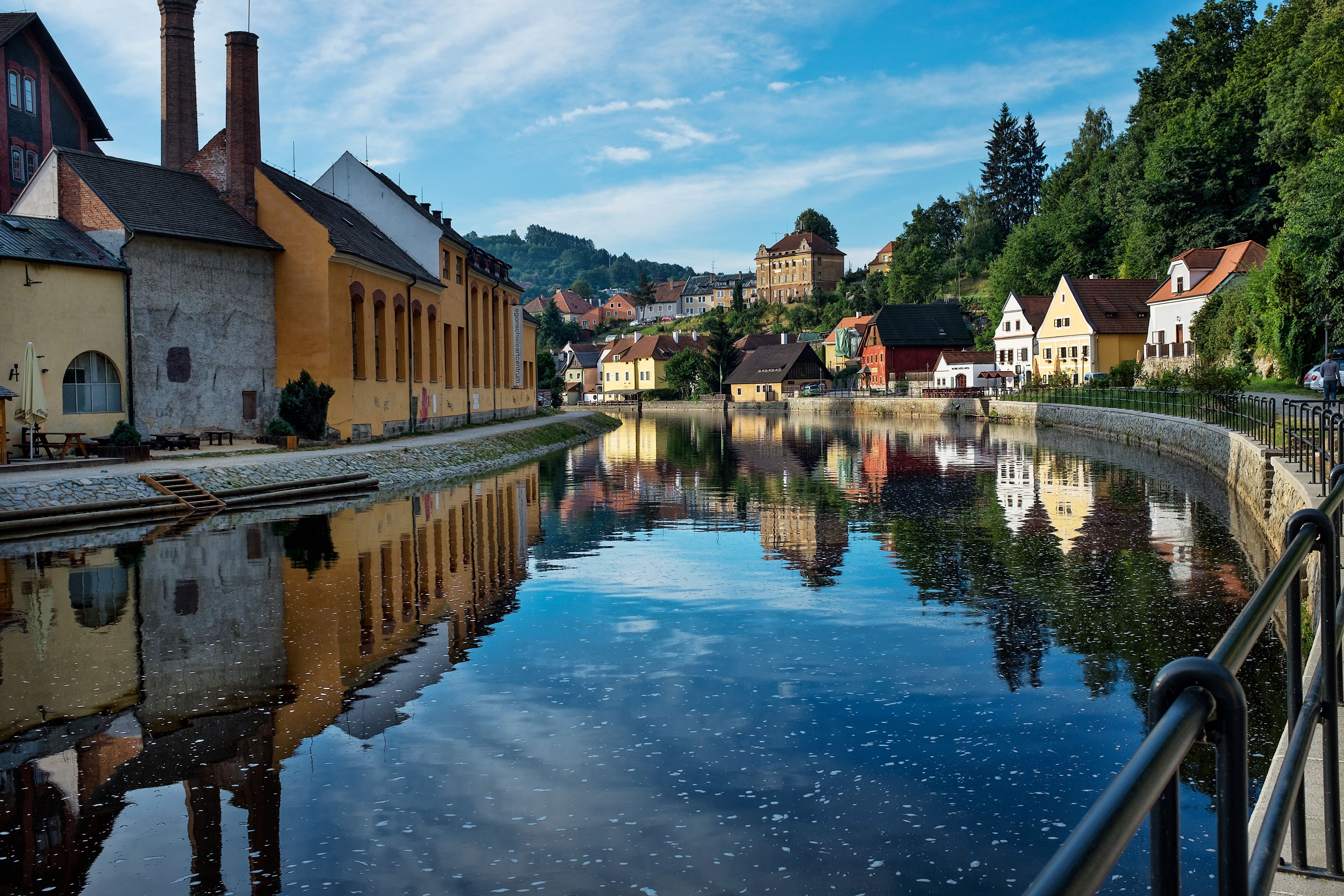 Dorfgebäude spiegeln sich im Wasser der Moldau in Cesky Krumlov bei blauem Himmel.
