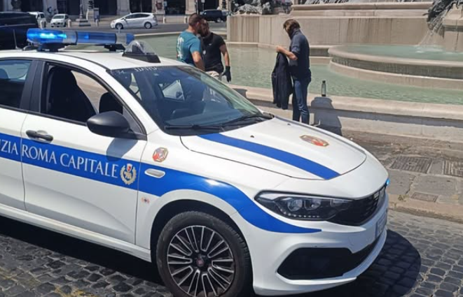 Polizeiauto der Polizia Roma Capitale steht vor einem Brunnen in Rom, zwei Personen nahe am Wasser.