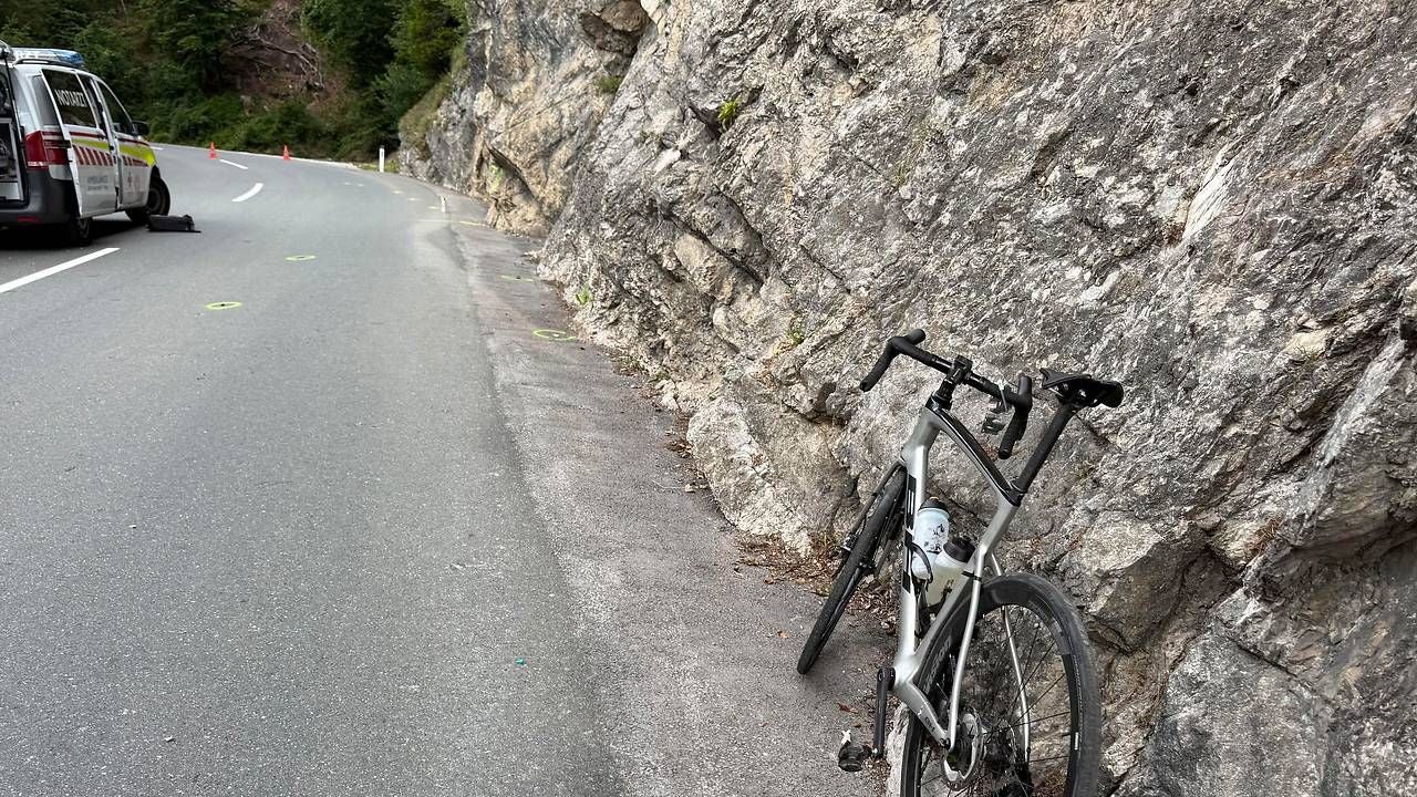 Rennrad lehnt an einer Felswand, Polizeiauto steht auf Straße mit Kurve in Kramsach.