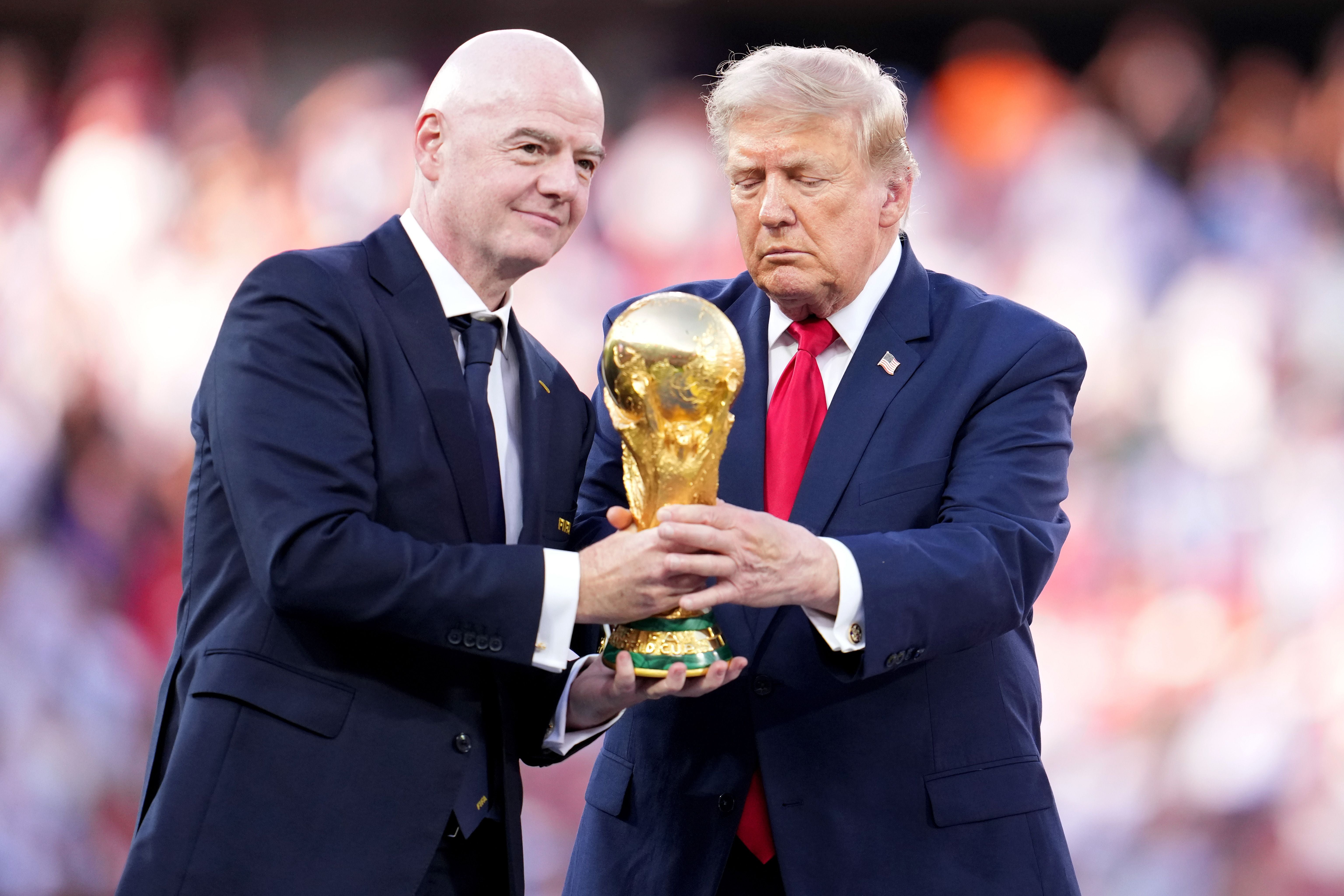 Zwei Männer im Anzug halten gemeinsam den FIFA-WM-Pokal bei einer Zeremonie.