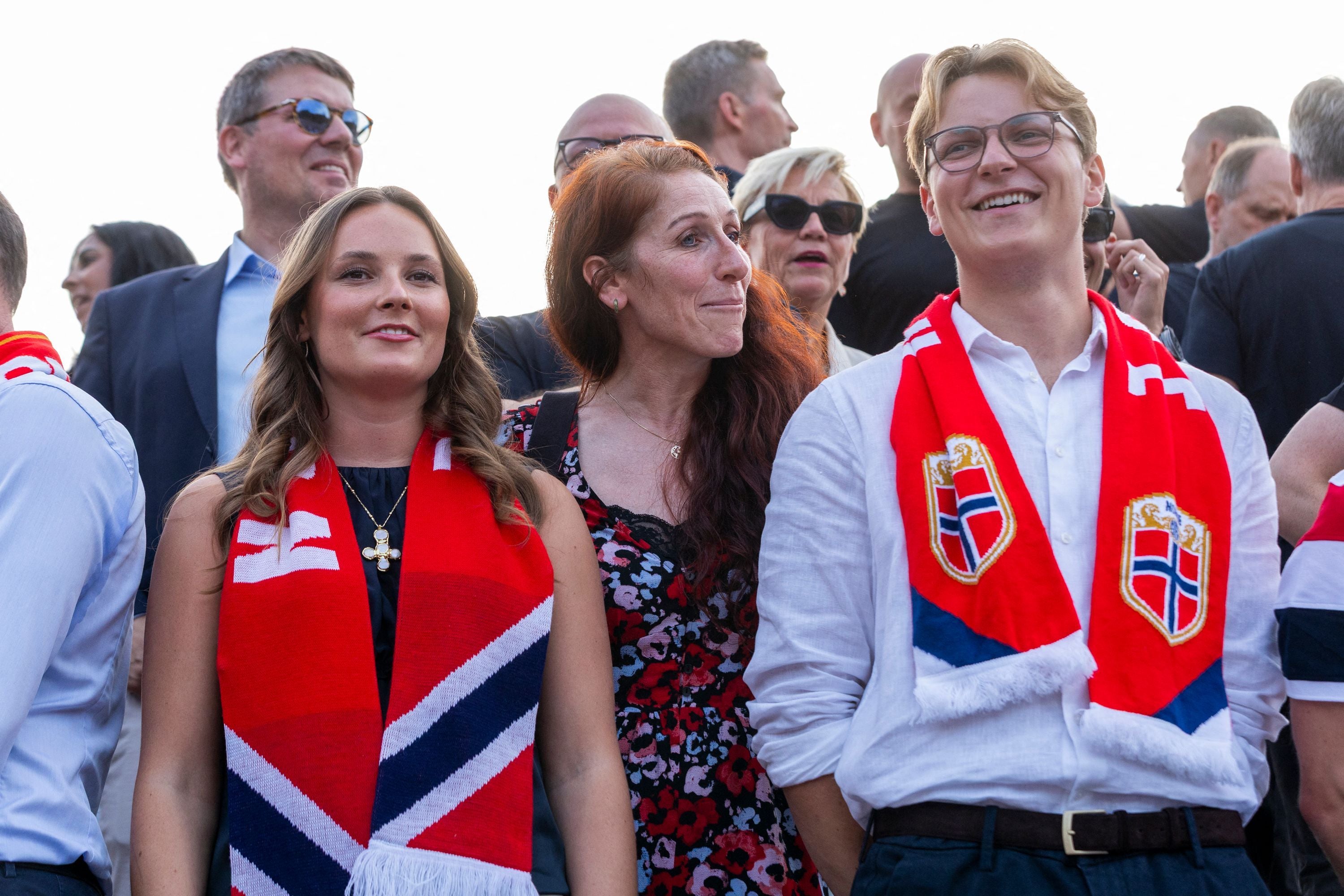 Fans mit roten Norwegen-Schals feiern gut gelaunt in einer Menschenmenge bei Tageslicht.