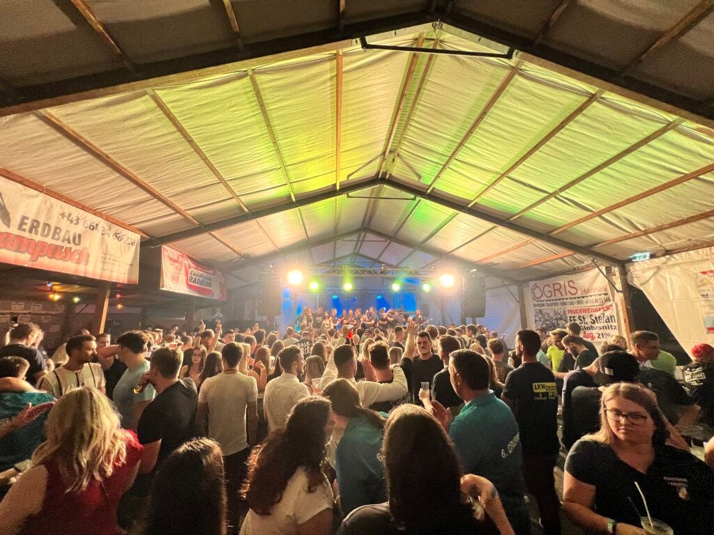 Viele Menschen feiern bei einem Feuerwehrfest in einem festlich beleuchteten Zelt.