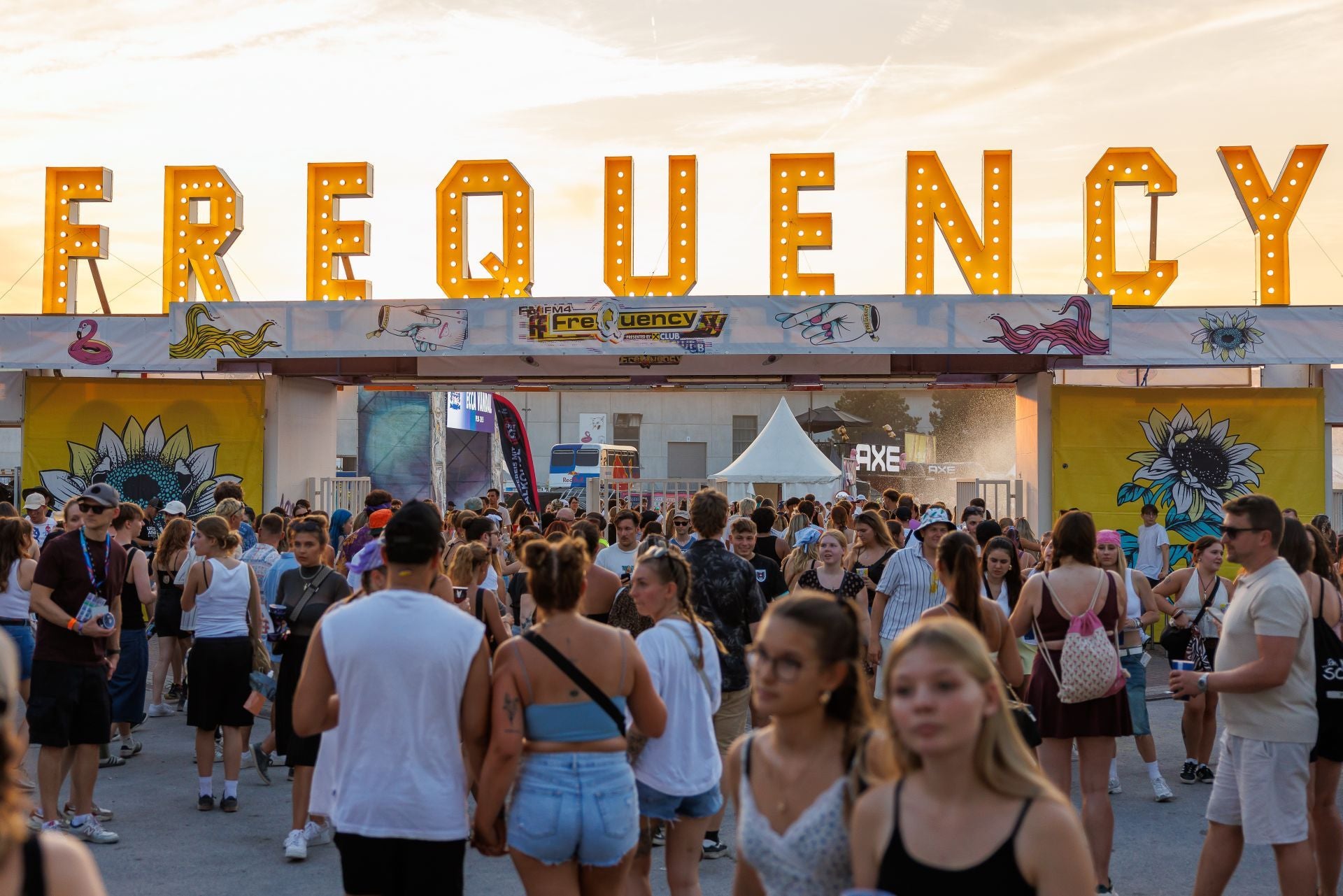 Viele Menschen gehen am Eingang des Frequency Festivals unter einem großen beleuchteten Schild.