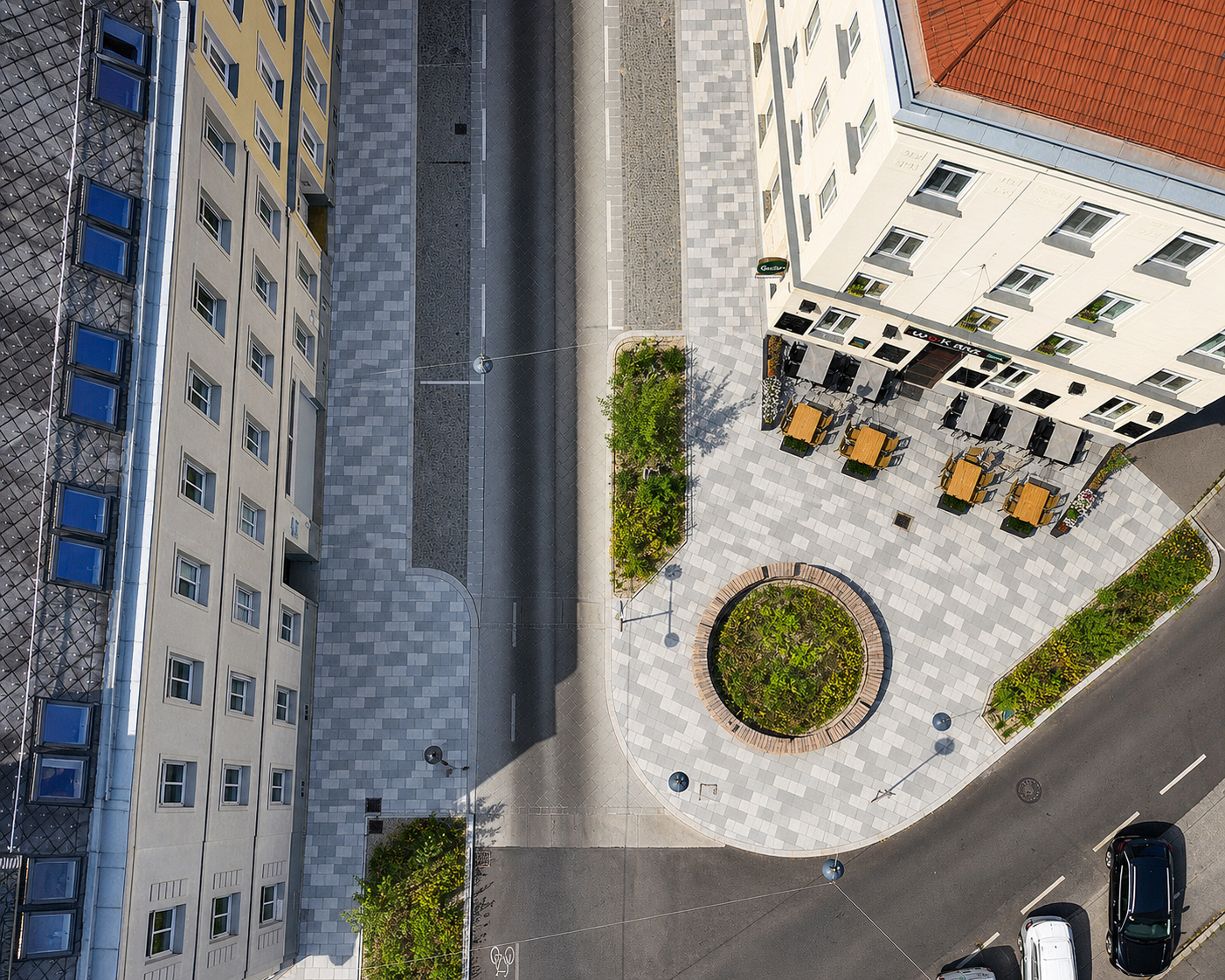 Luftaufnahme einer umgestalteten Straße mit Sitzplätzen, Begrünung und modernen Gehwegen.