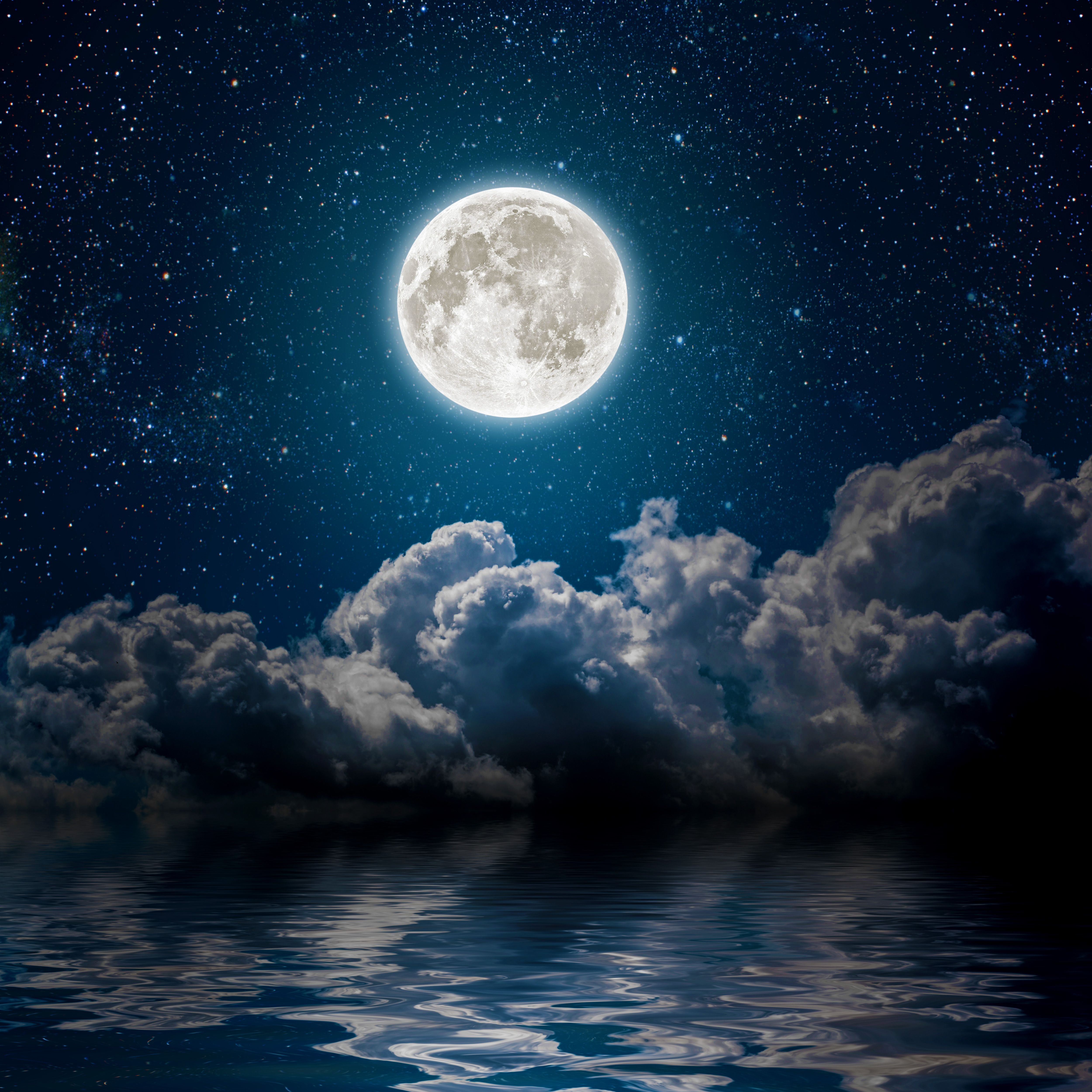 Vollmond am sternklaren Himmel spiegelt sich im ruhigen Meer, umgeben von Wolken.