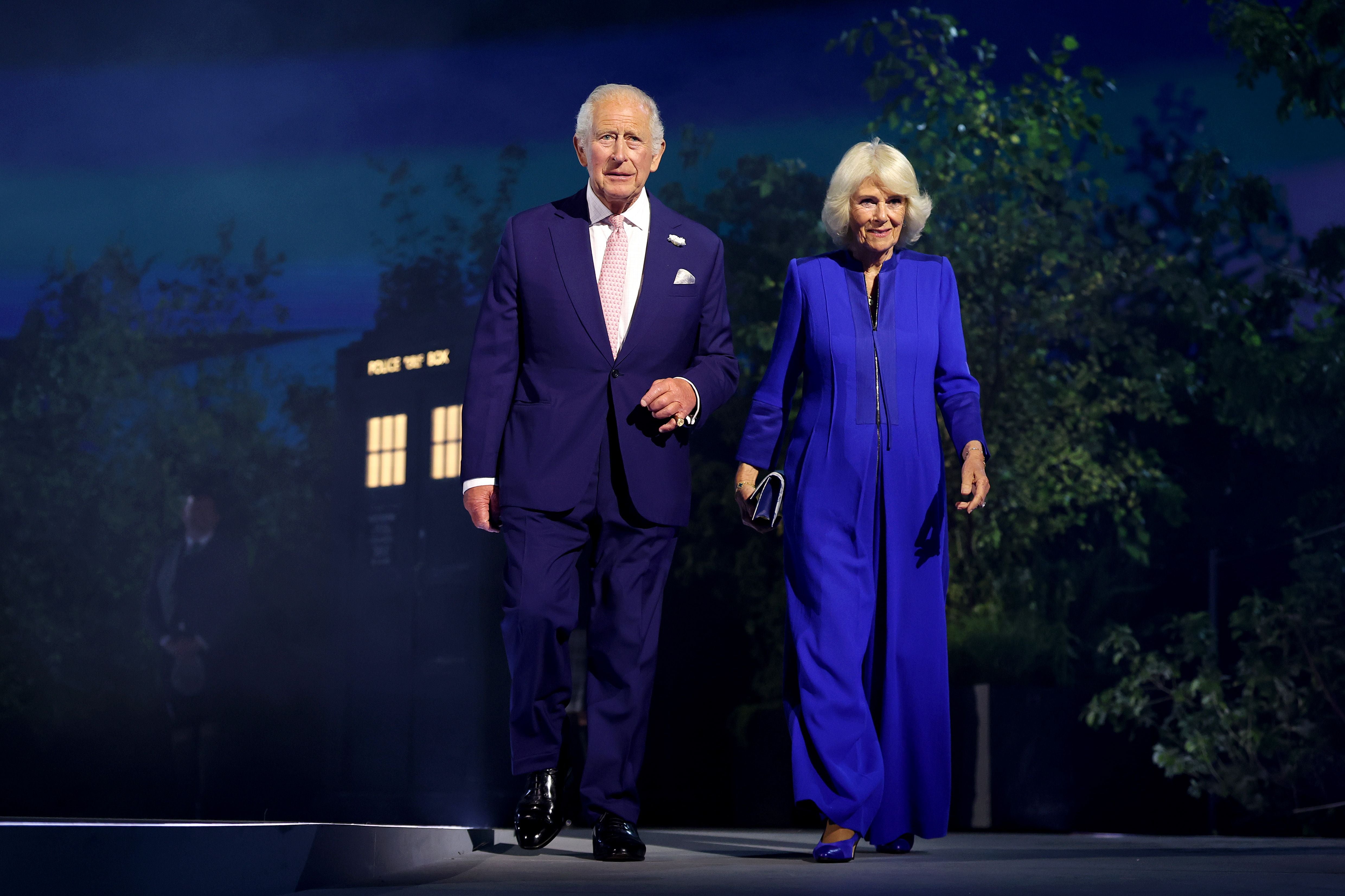 Ein älterer Mann und eine Frau in blauer Kleidung gehen gemeinsam über eine beleuchtete Bühne.