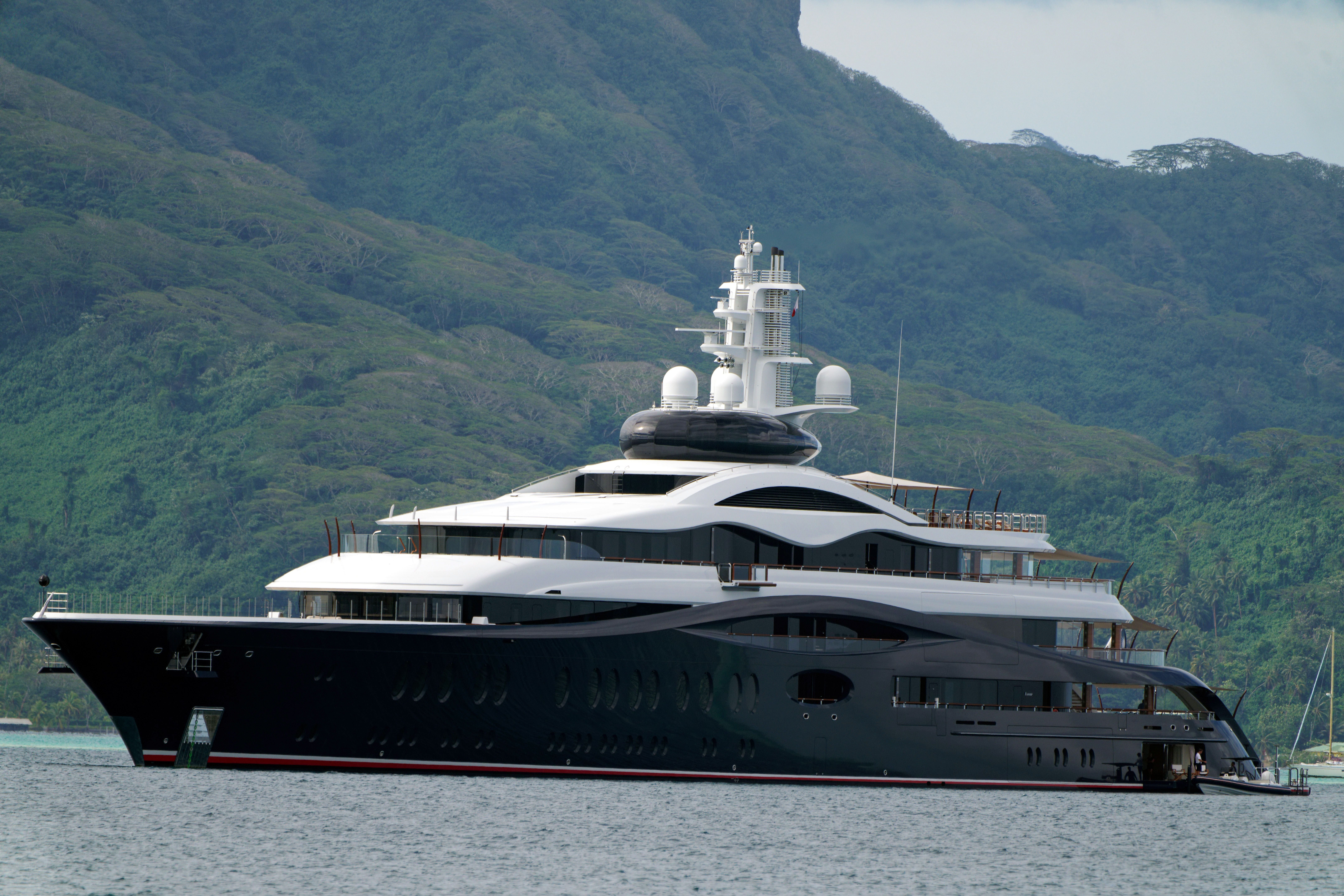 Große luxuriöse Yacht ankert vor einer grünen, bergigen Küste in Französisch-Polynesien.