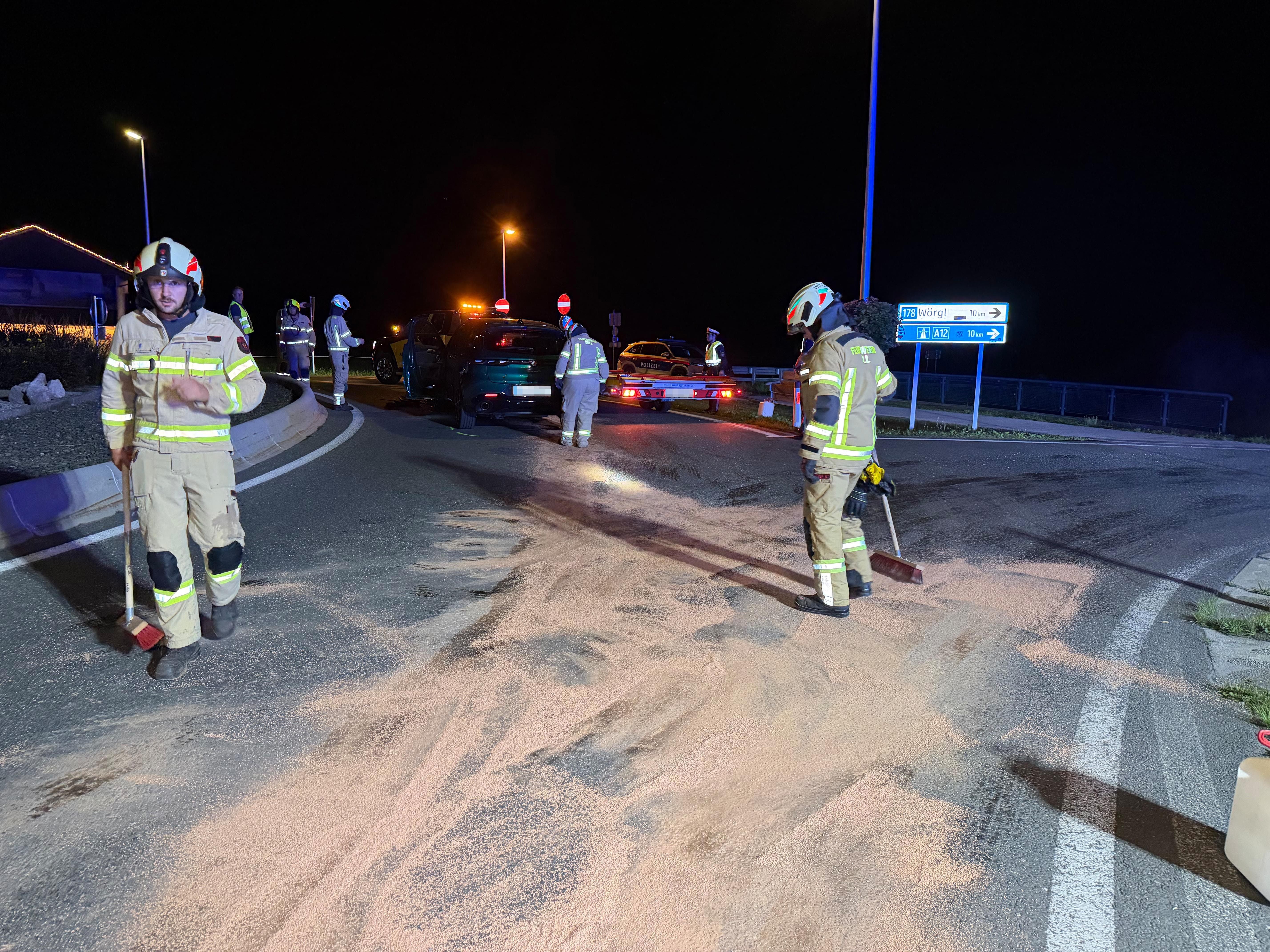 Feuerwehrleute sichern nachts eine Unfallstelle und streuen Bindemittel auf die Straße.