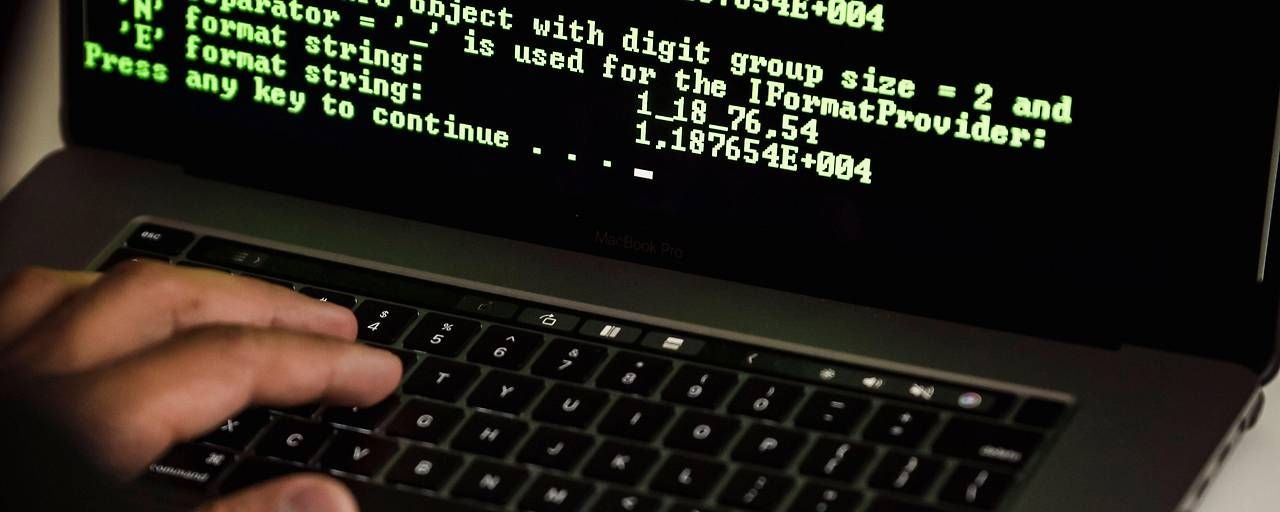 Hand tippt auf Laptop mit grünem Programmiercode auf schwarzem Bildschirm.