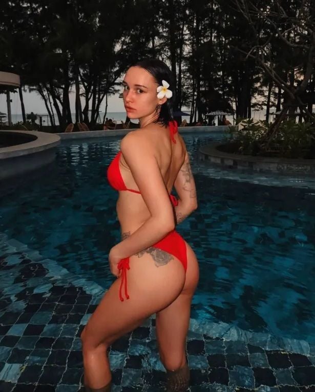 Frau im roten Bikini steht am Beckenrand eines Pools mit Blume im Haar.