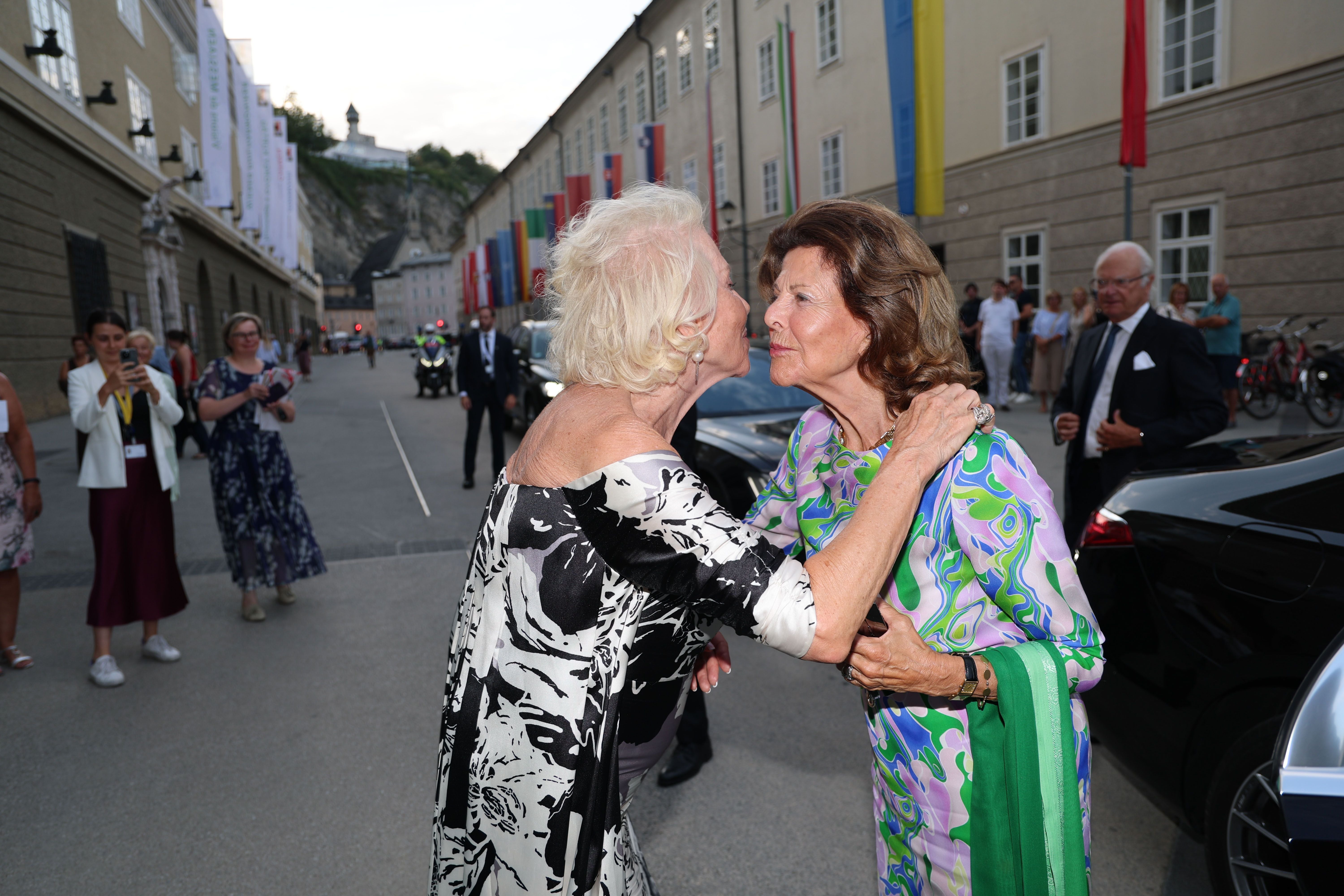 Zwei elegant gekleidete Frauen begrüßen sich herzlich vor einem Festspielhaus in Salzburg.
