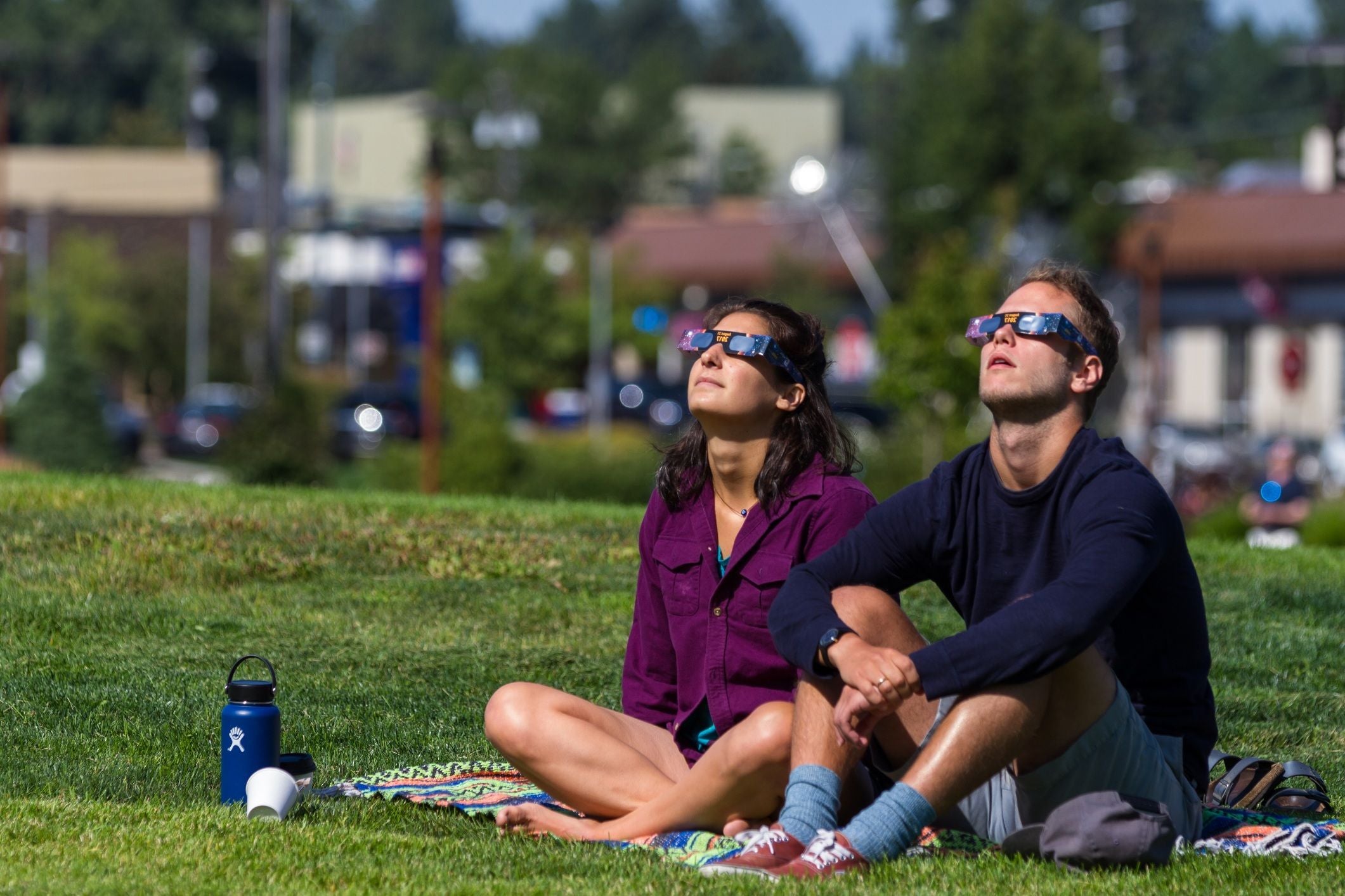 Ein Paar sitzt mit Schutzbrillen auf einer Wiese und beobachtet gemeinsam eine Sonnenfinsternis.