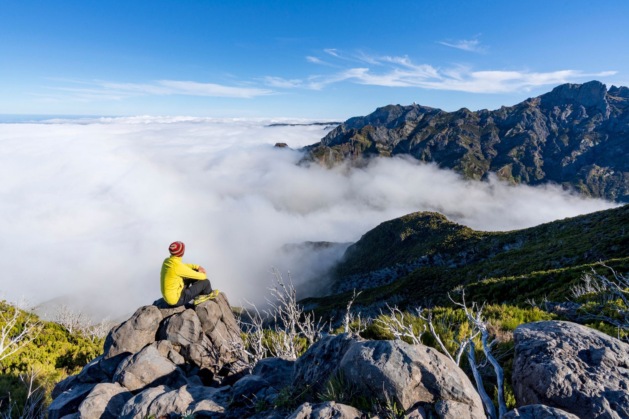 Mann sitzt auf Felsen und blickt auf nebelverhangene Berge in Madeira, Portugal.