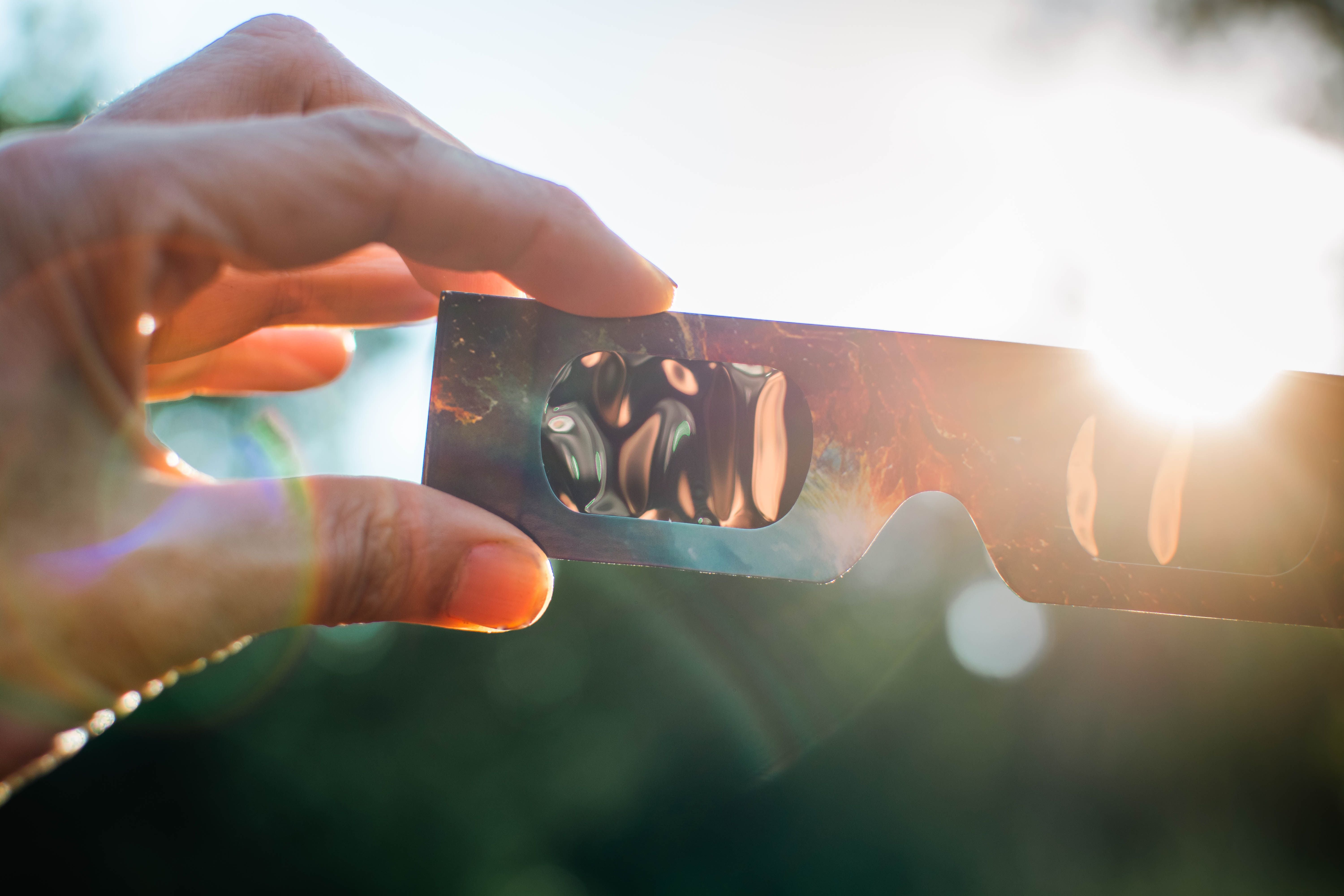 Hand hält Sonnenfinsternisbrille vor die Sonne, Sonnenlicht scheint durch die Gläser.