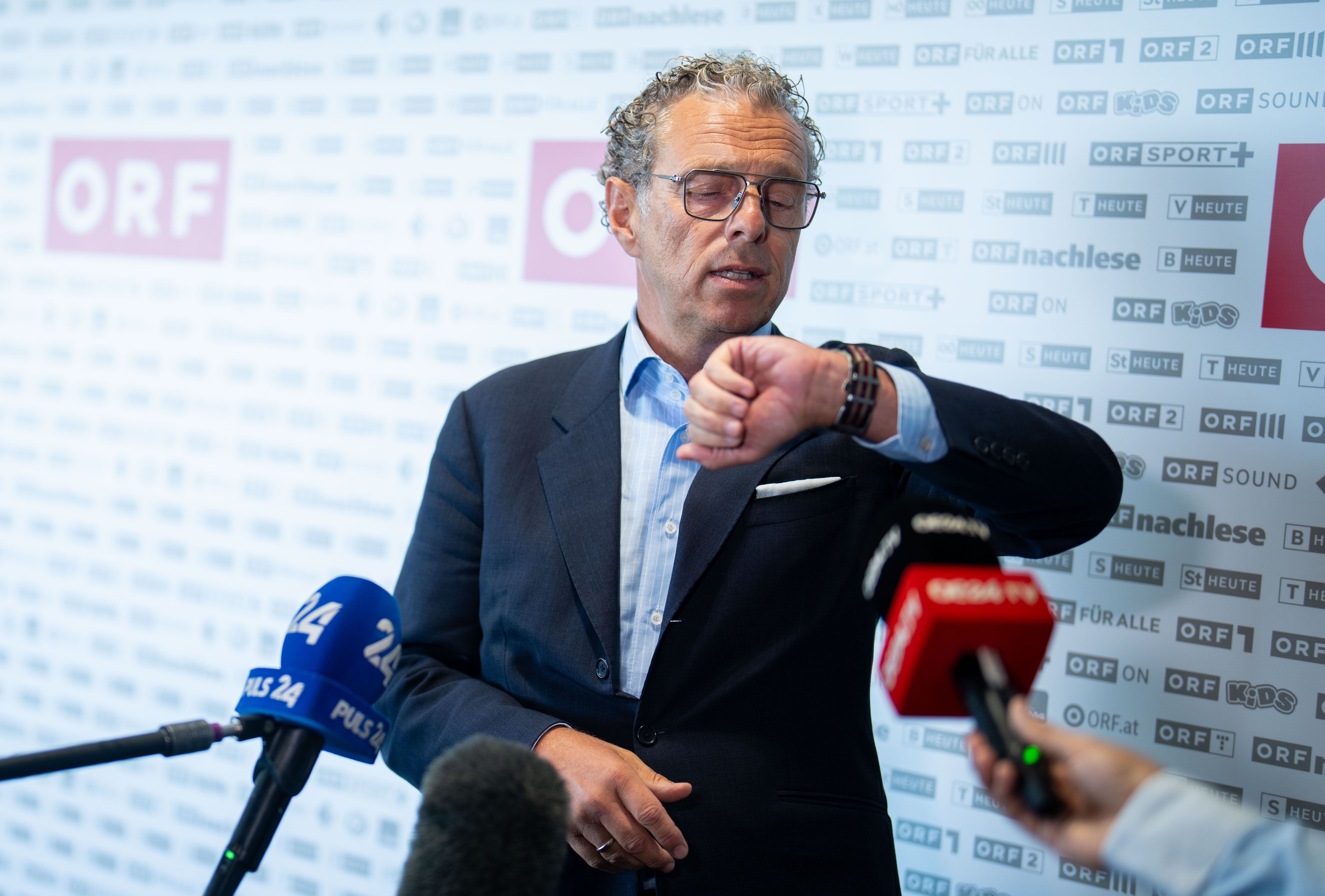 Ein Mann im Anzug blickt während einer Pressekonferenz auf seine Armbanduhr.